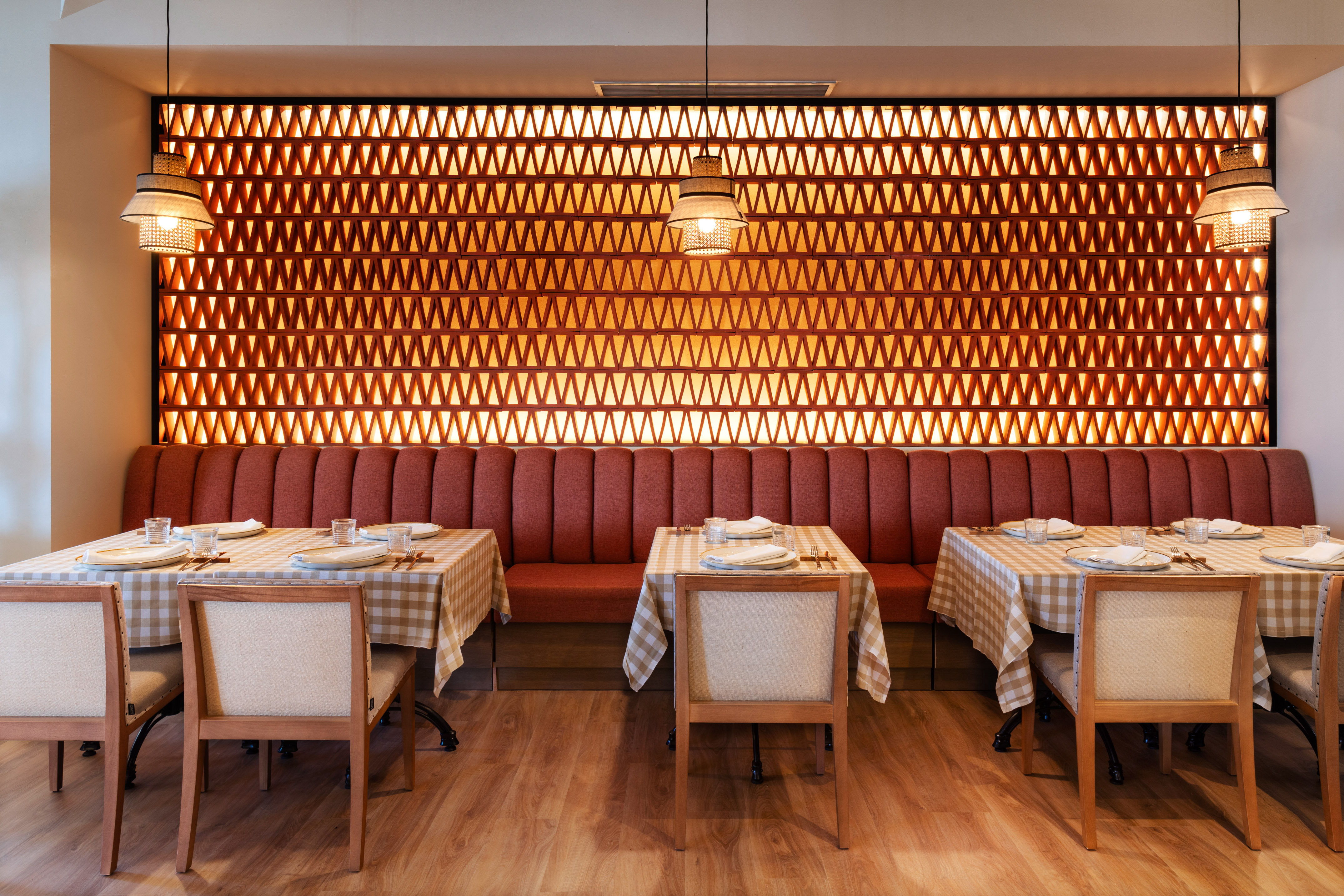 Modern restaurant dining with geometric wall panel, red banquette, and set tables.