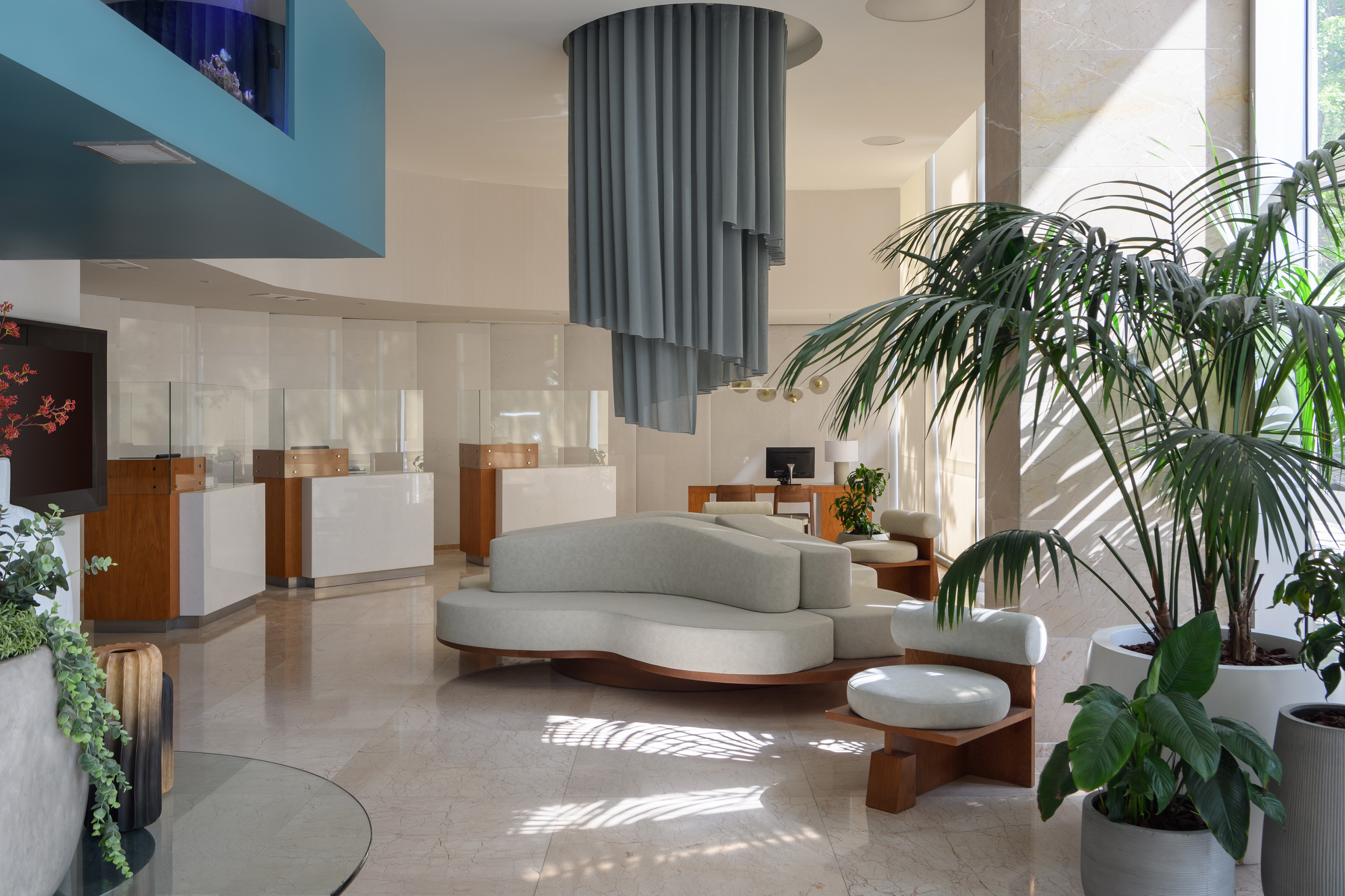 Luxury hotel lobby with curved sofa, tropical plants, and ceiling aquarium.