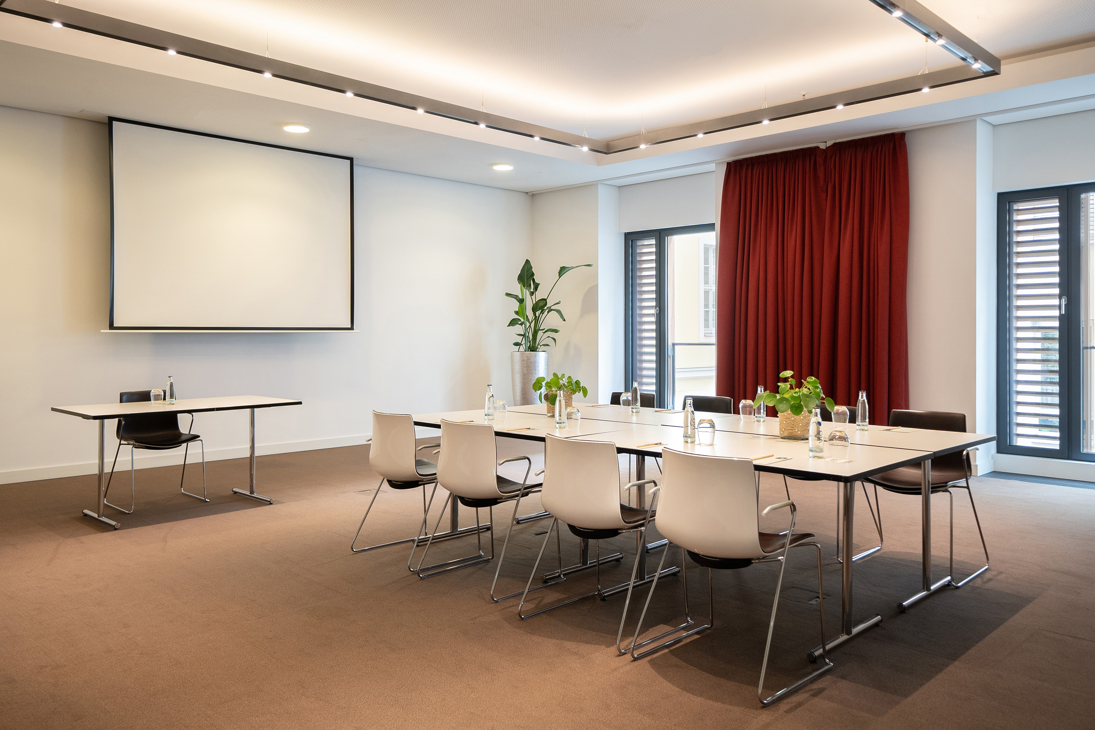 Modern meeting room with projector screen, tables, chairs, and red curtains. - CONEins - INNSiDE Dresden, Dresden