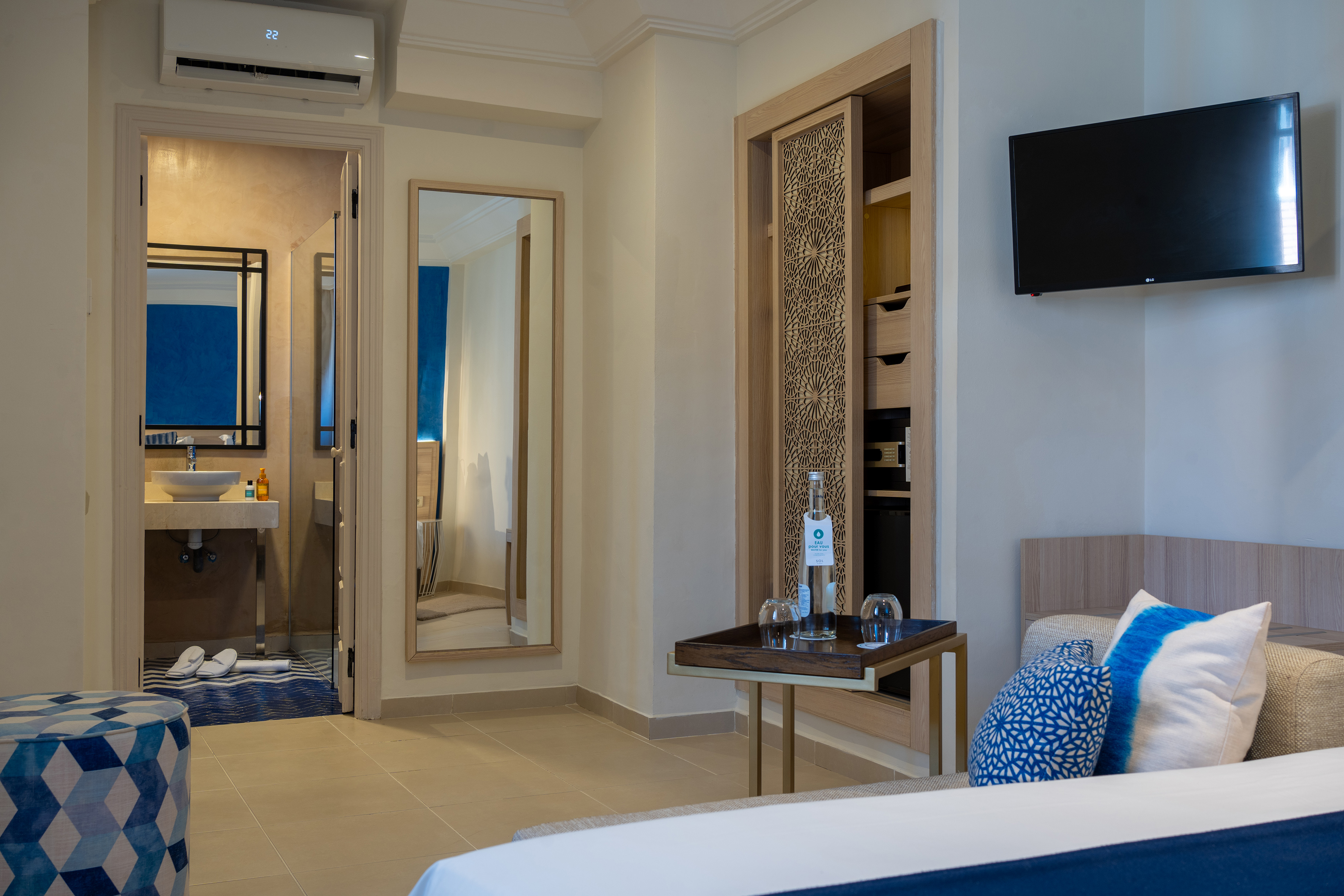 Modern hotel room with blue accents, bed, TV, wardrobe, and bathroom.