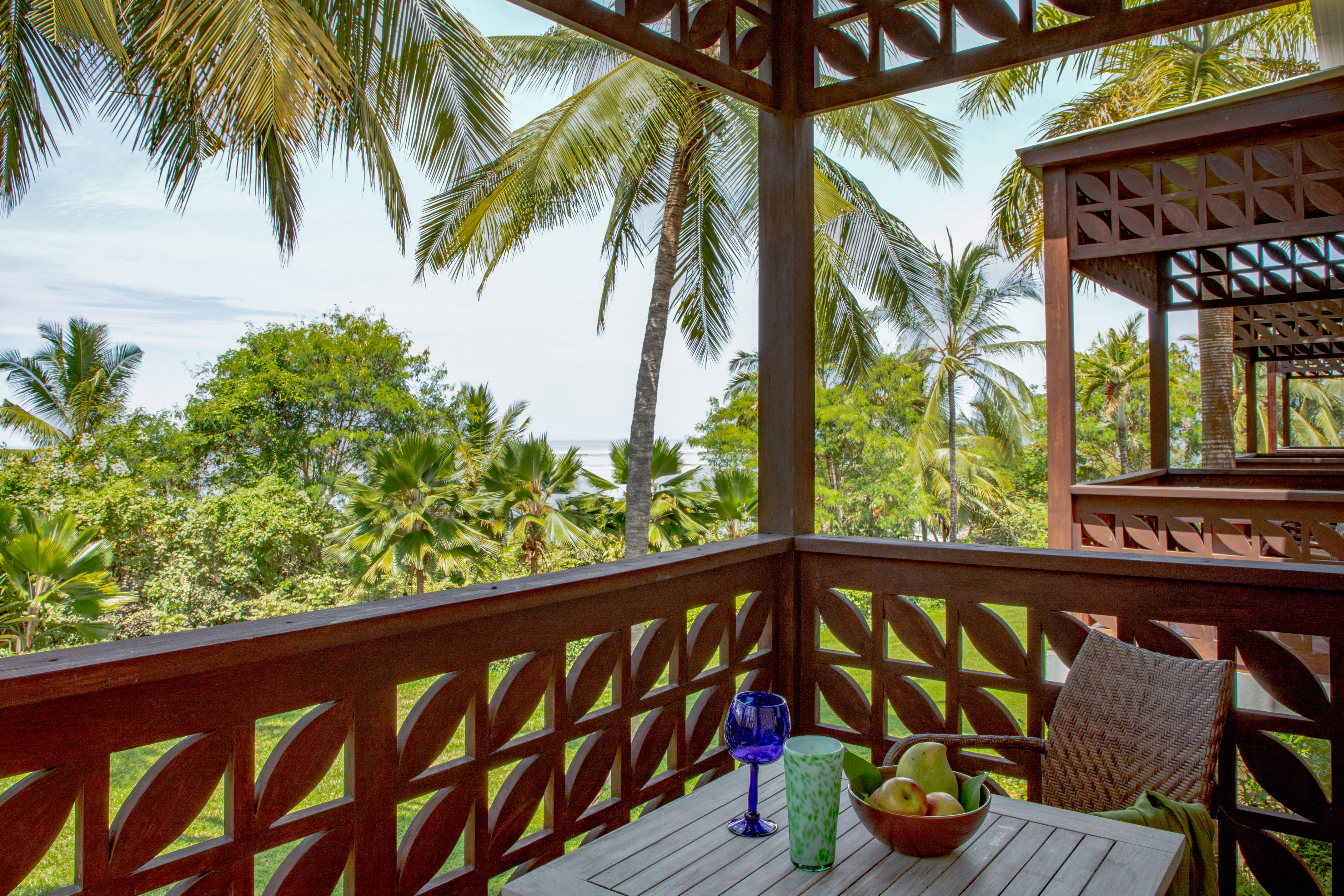 Tropical balcony with ocean view, palm trees, and wooden table with fruit.