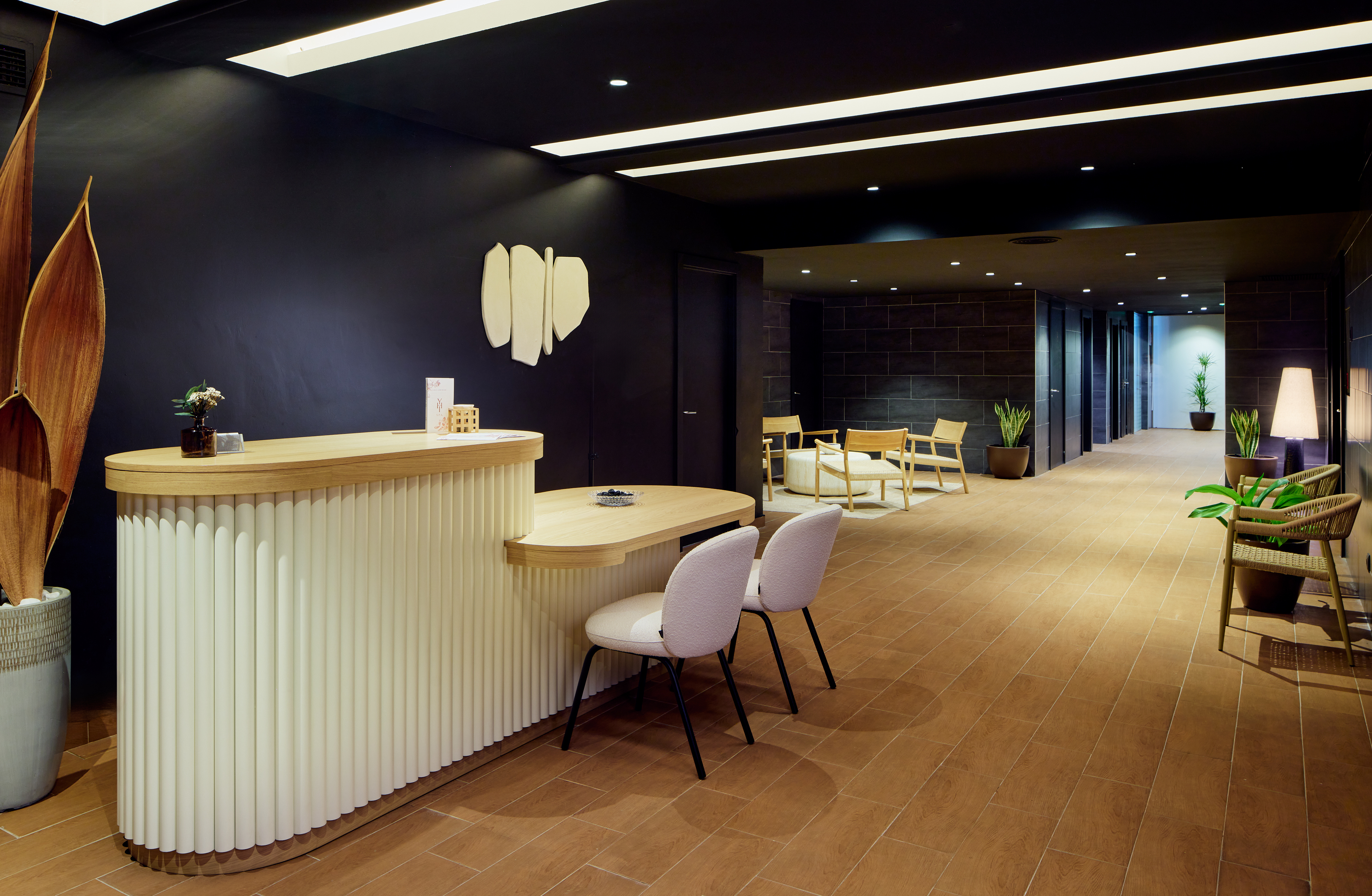 Fluted reception desk and modern lobby with seating, plants, and dark walls.
