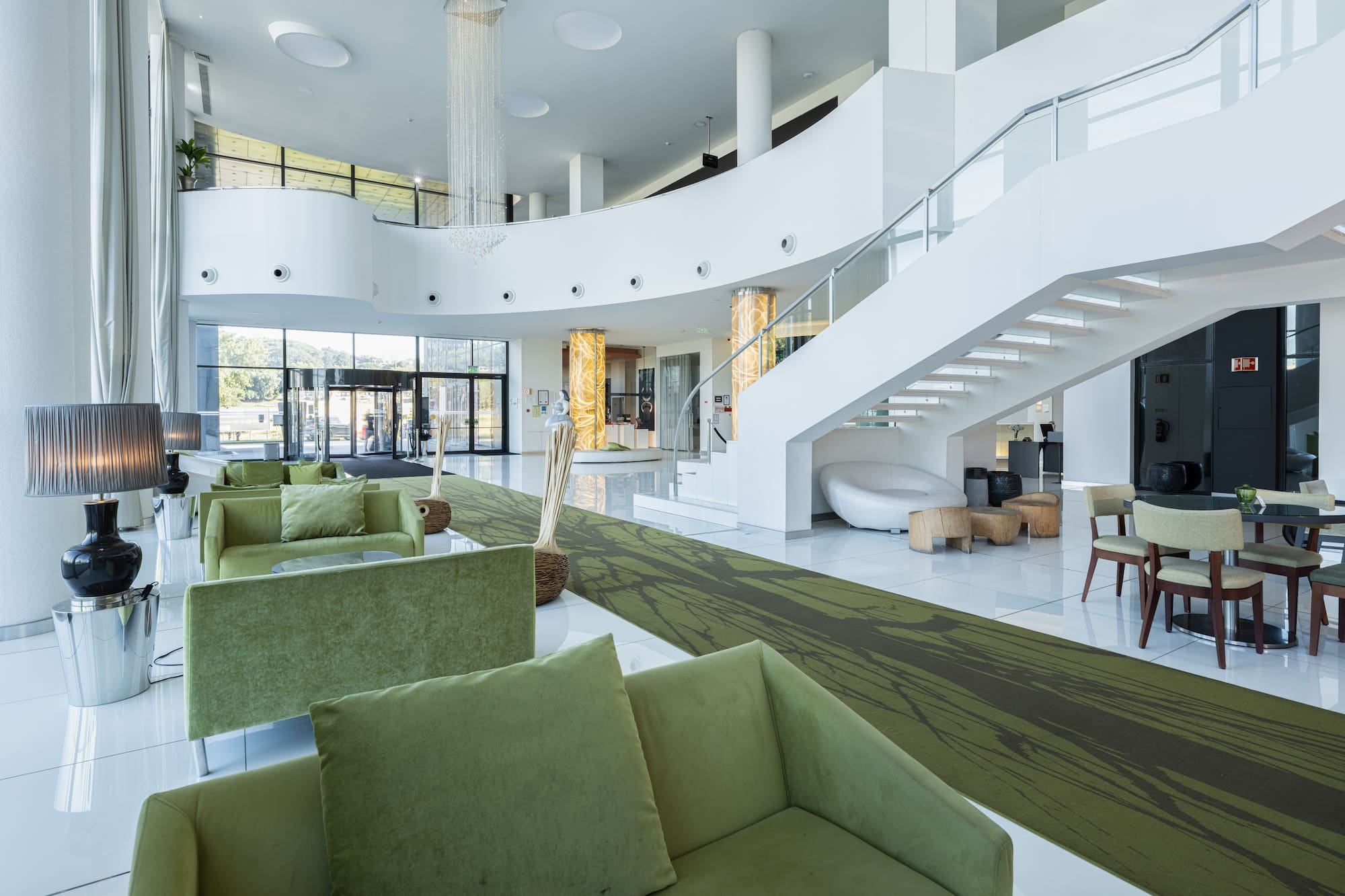 Modern hotel lobby with green sofas, white staircase, and elegant interior.