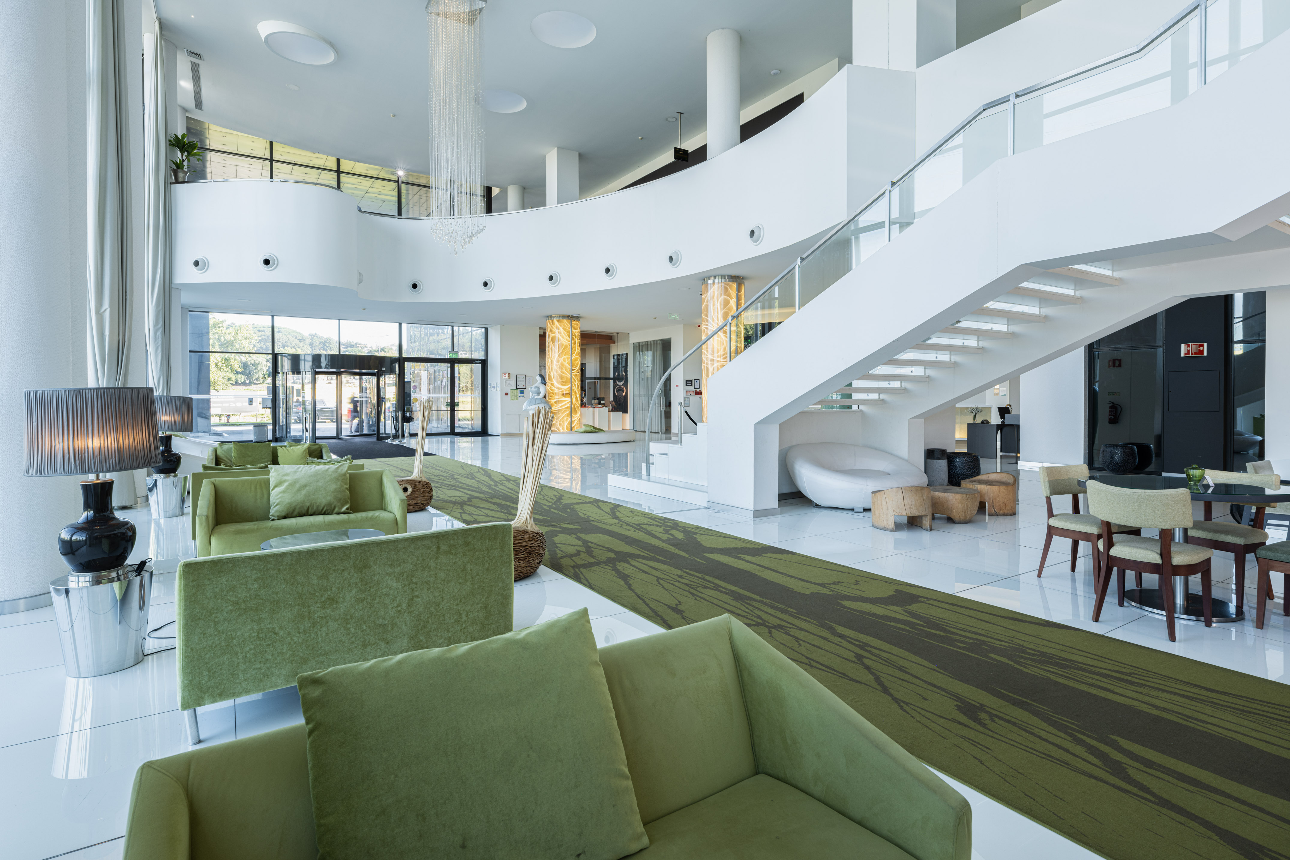 Modern hotel lobby with green sofas, white staircase, and elegant interior.