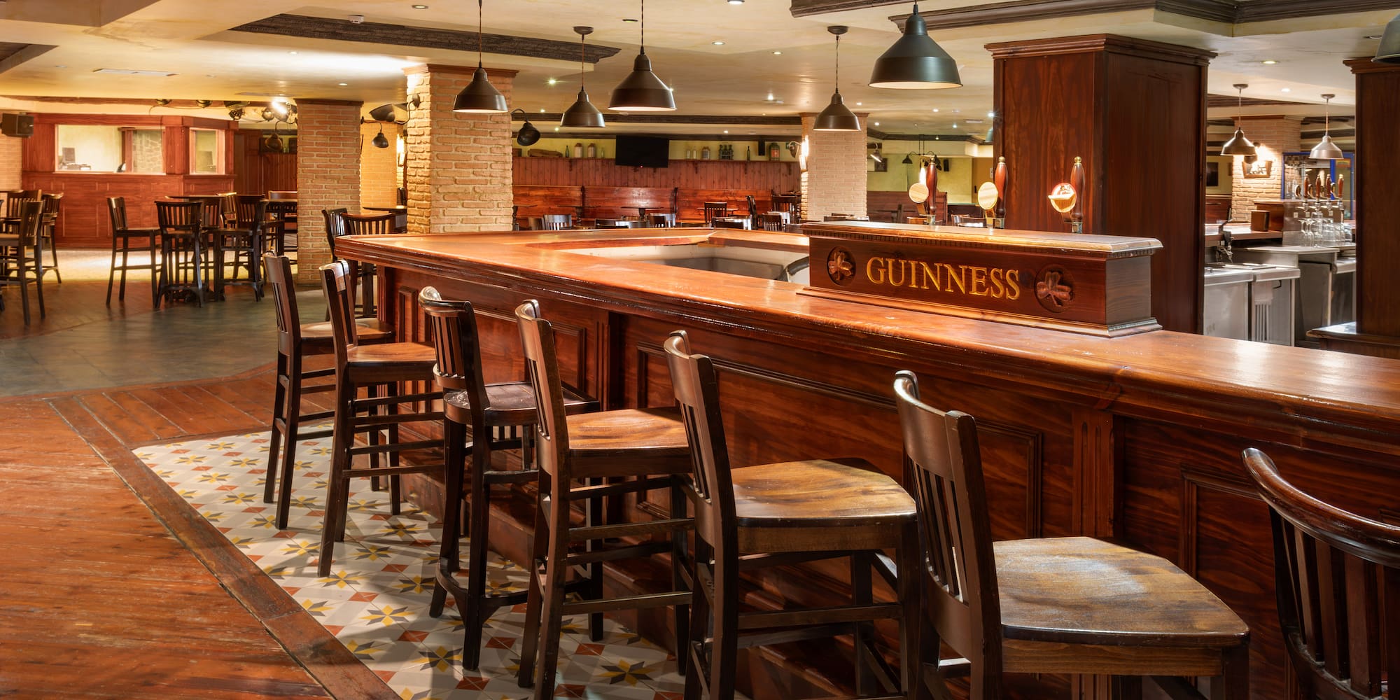 Guinness pub interior with dark wood bar, stools, patterned floor, and warm lighting.