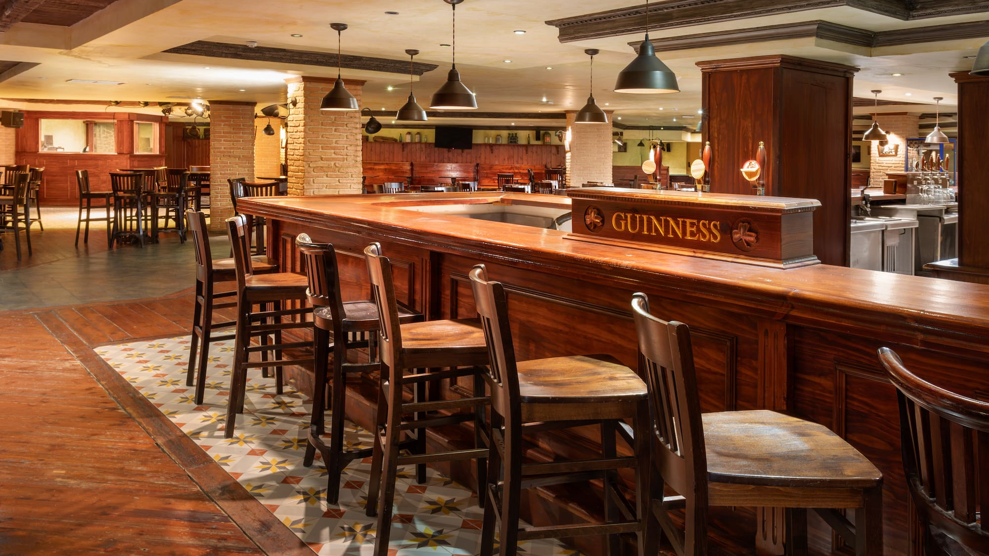 Guinness pub interior with dark wood bar, stools, patterned floor, and warm lighting.