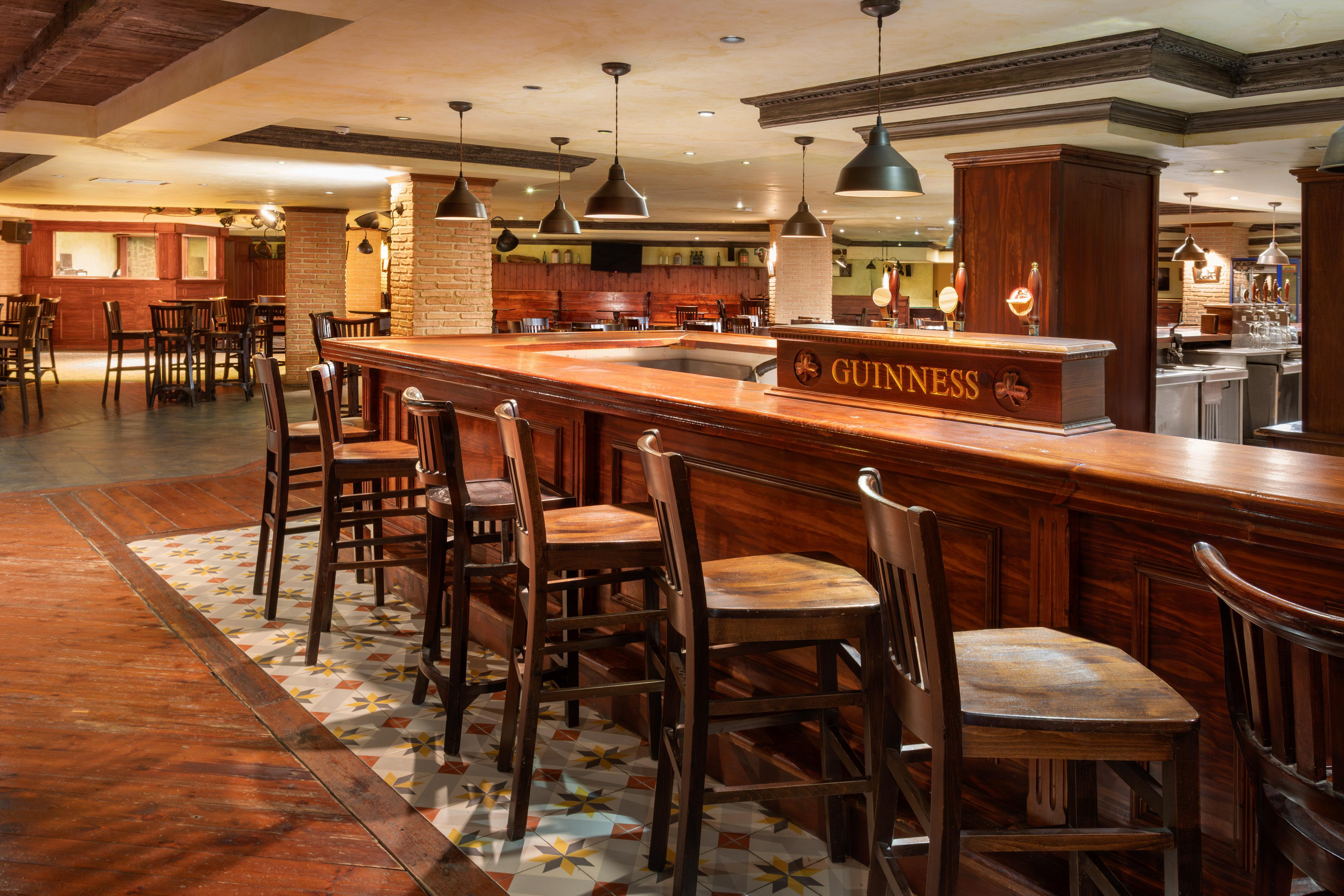 Guinness pub interior with dark wood bar, stools, patterned floor, and warm lighting.