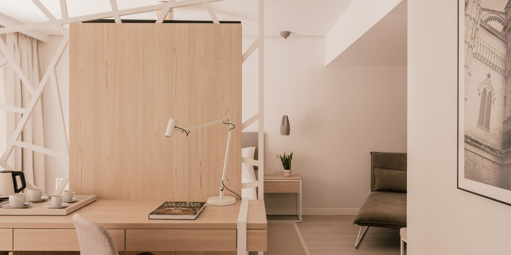 Modern hotel room with work desk, light wood, and geometric partition.