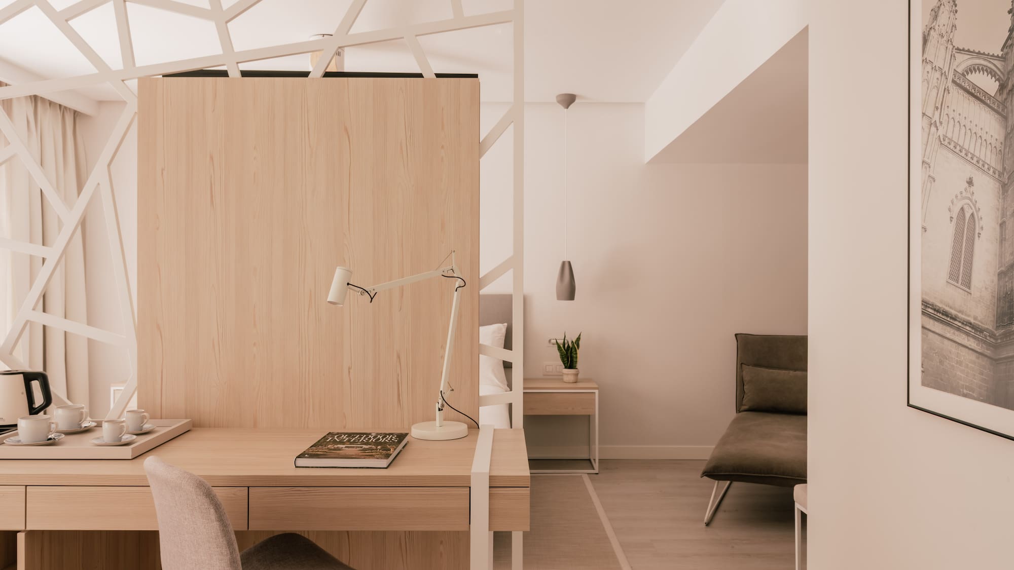 Modern hotel room with work desk, light wood, and geometric partition.