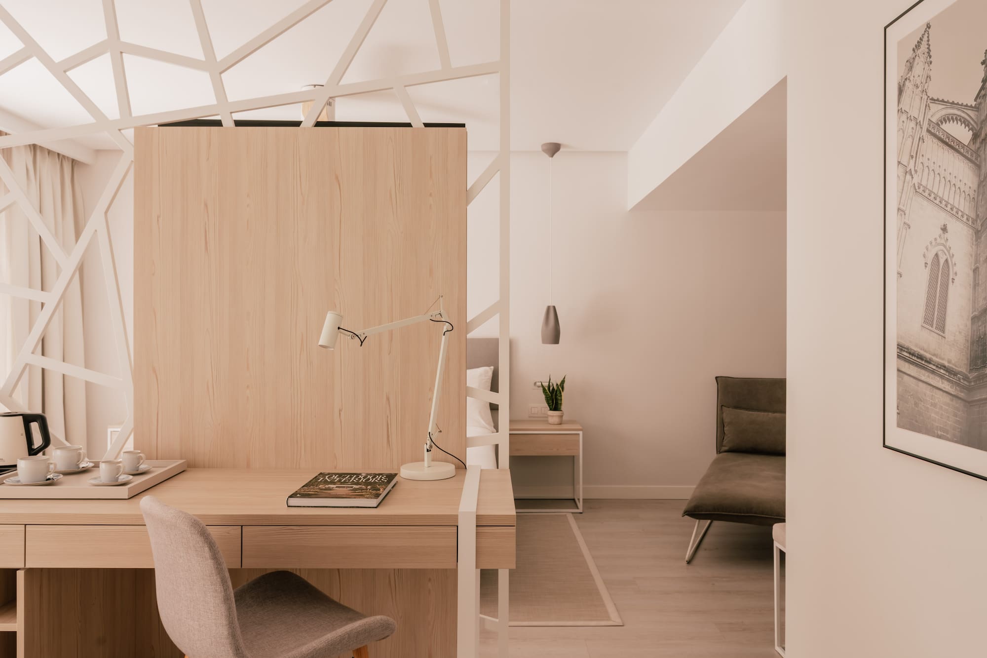 Modern hotel room with work desk, light wood, and geometric partition.
