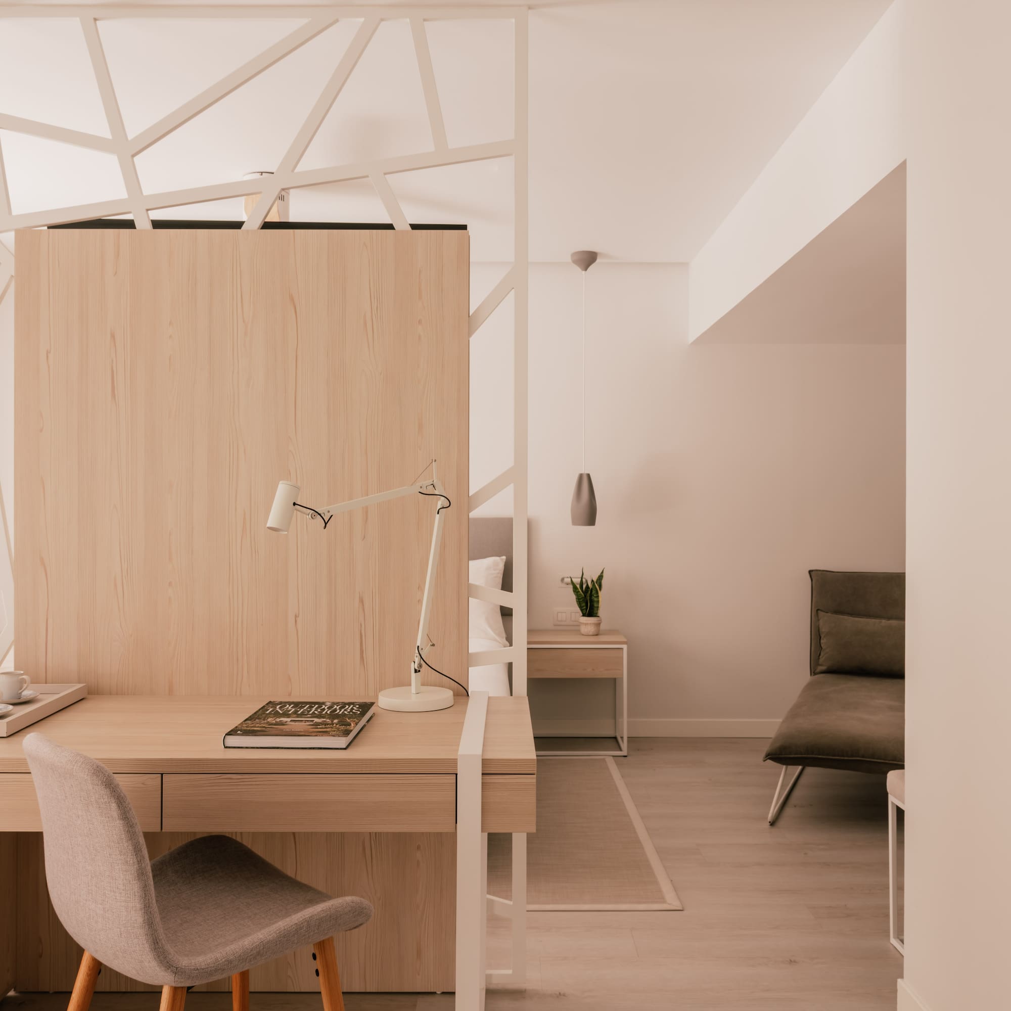 Modern hotel room with work desk, light wood, and geometric partition.