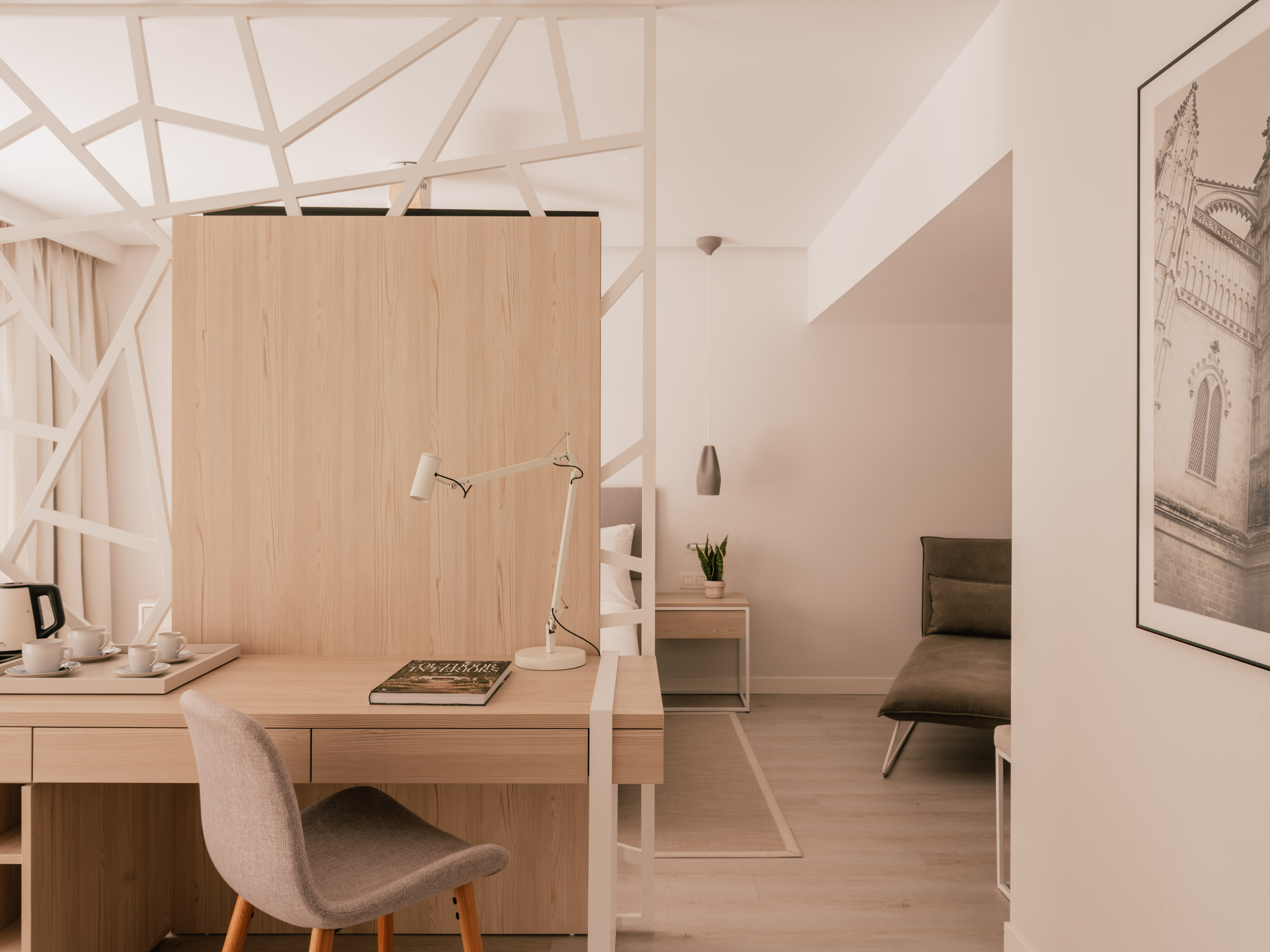 Modern hotel room with work desk, light wood, and geometric partition.