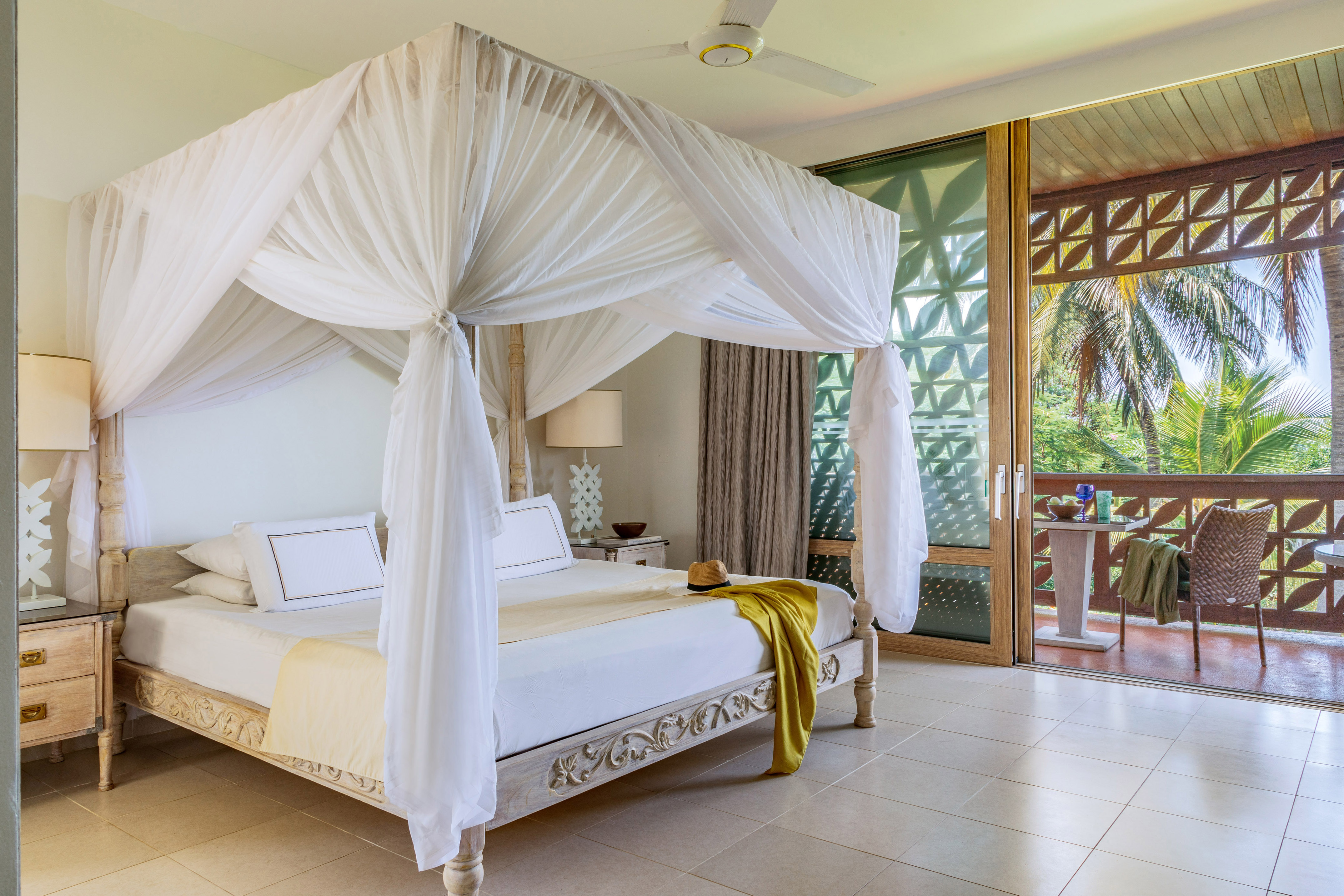 Elegant tropical bedroom with carved canopy bed and balcony overlooking palms.