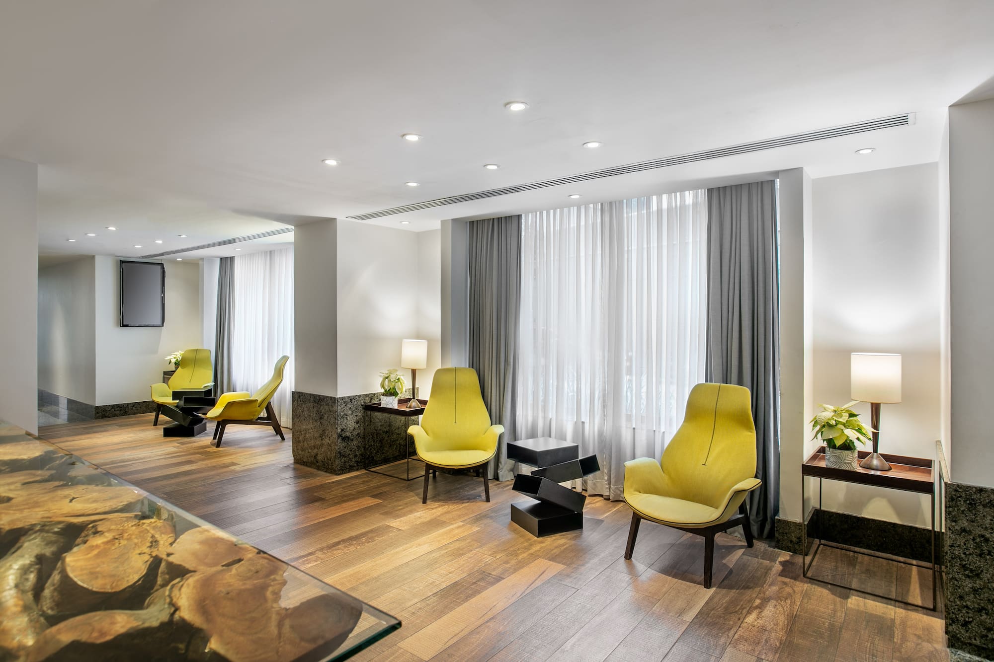 Modern lounge with yellow armchairs, hardwood floor, and recessed lighting.