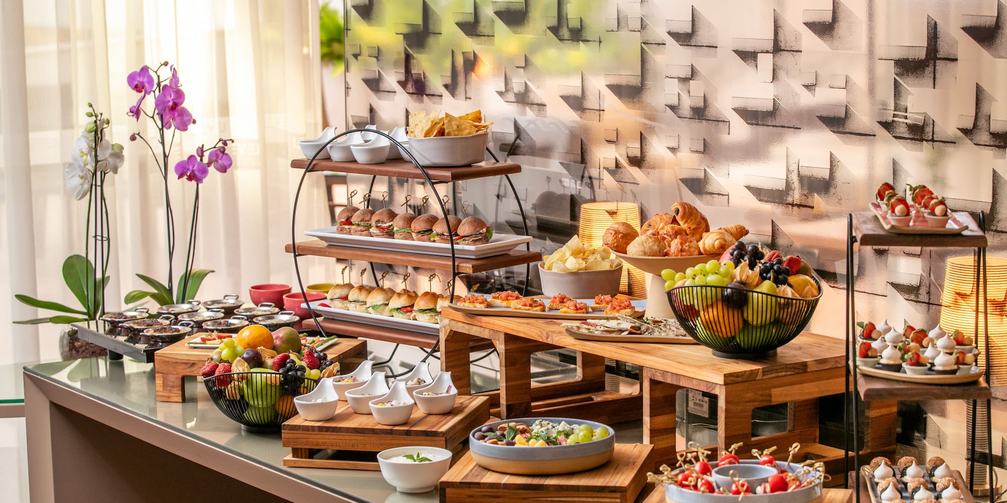 Diverse catering buffet featuring sliders, croissants, fresh fruit, and sweet treats.