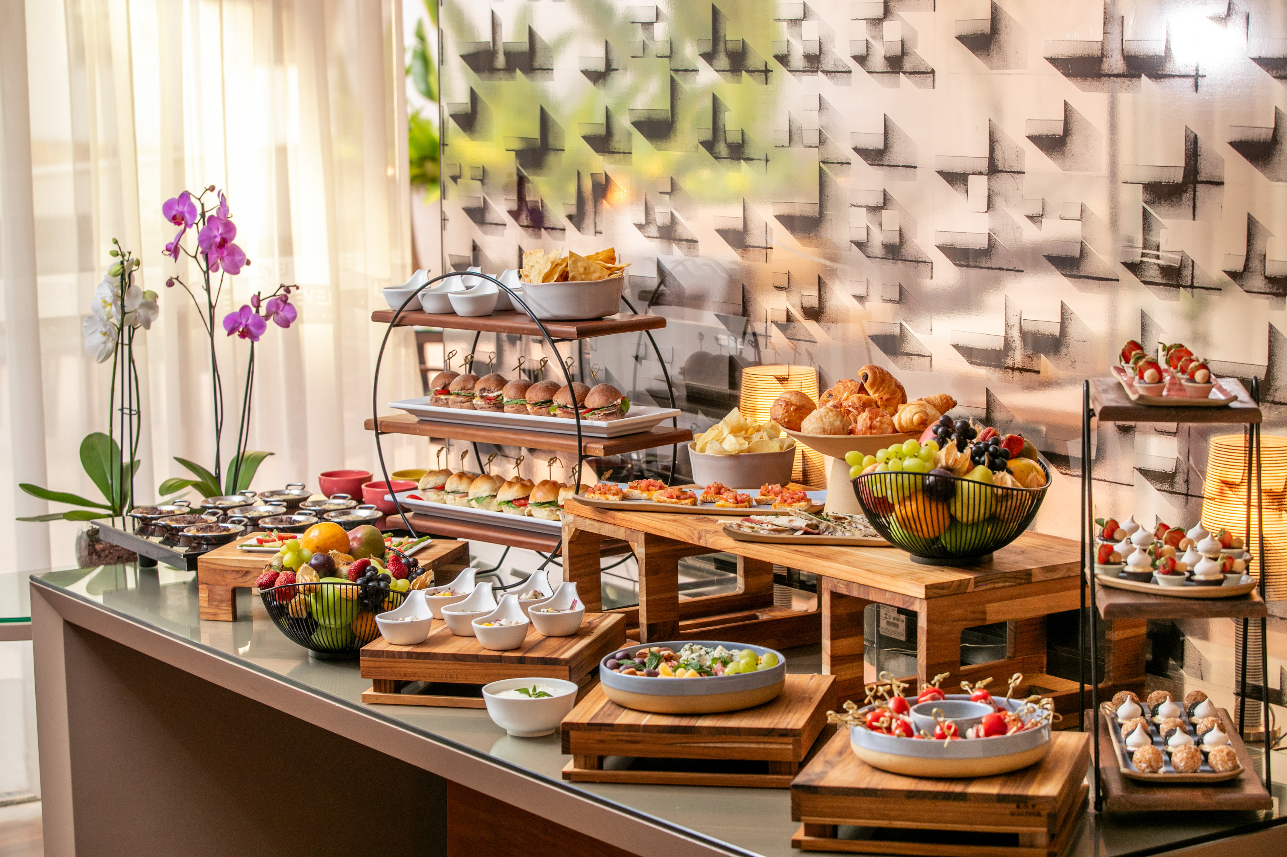 Diverse catering buffet featuring sliders, croissants, fresh fruit, and sweet treats.