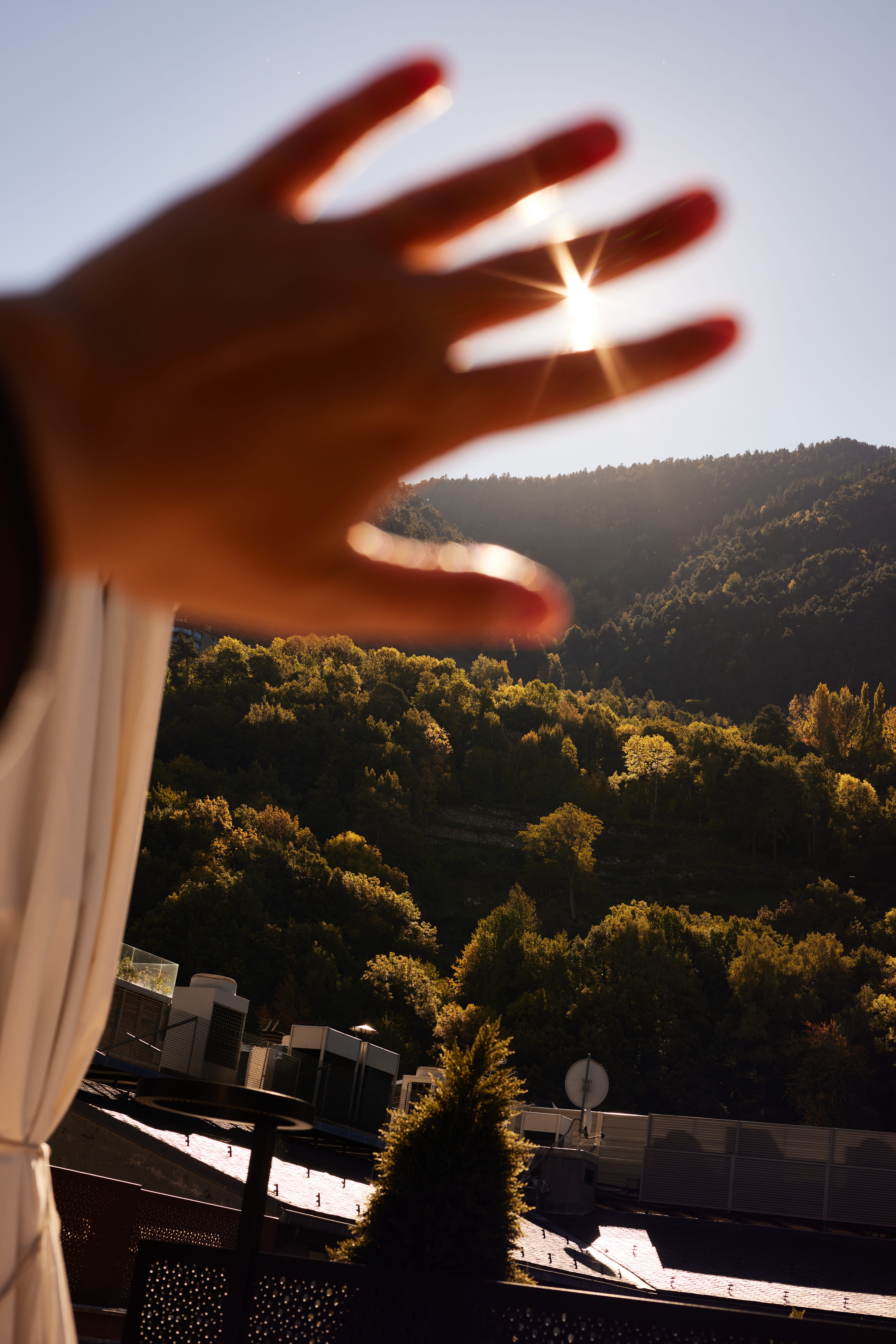 Hand shielding bright sun over a green mountain forest.