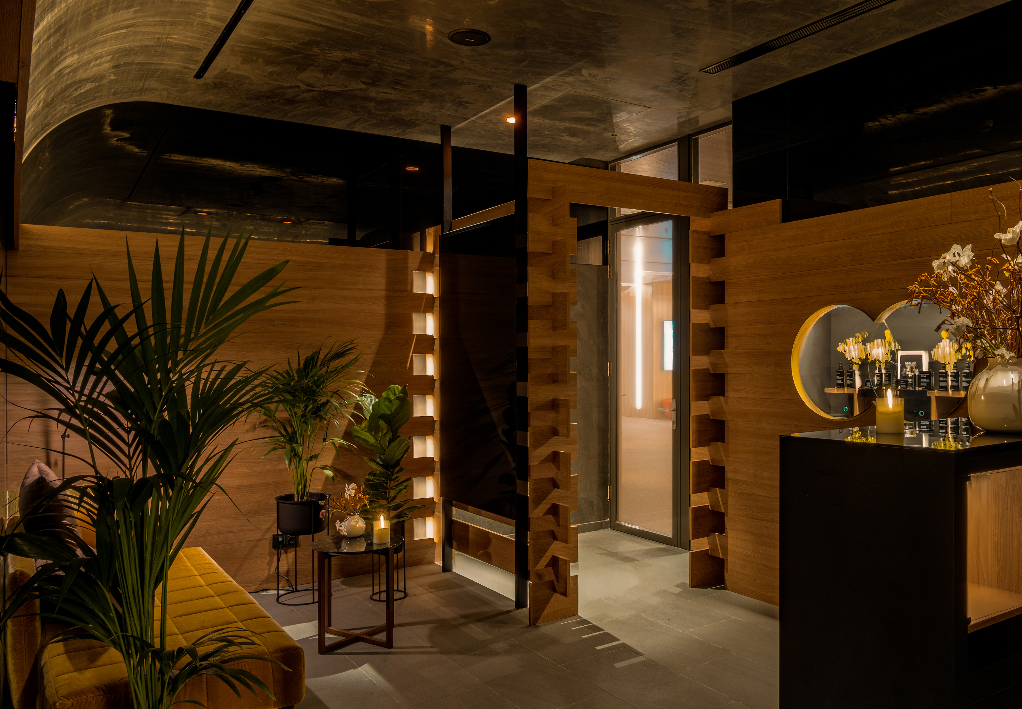 Modern spa waiting area with warm wood panels, lush plants, and retail display.