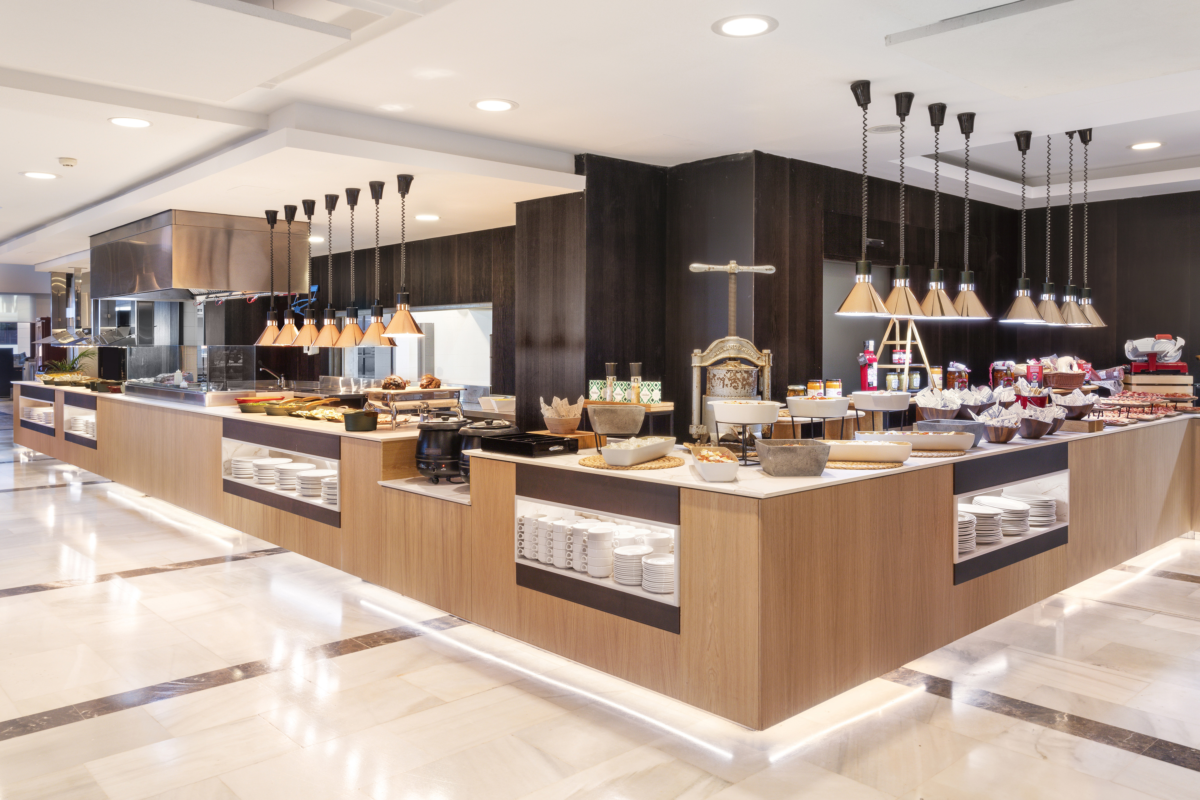 Modern hotel buffet with various food, warming lamps, and serving dishes.