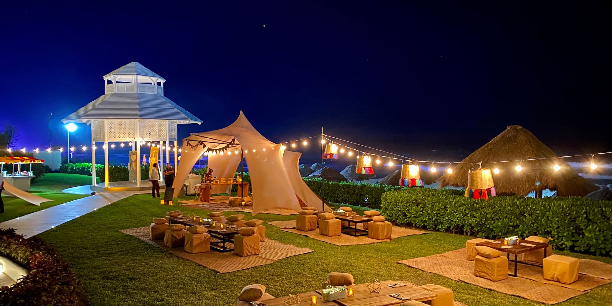 a group of tables and chairs in a yard with lights and a gazebo