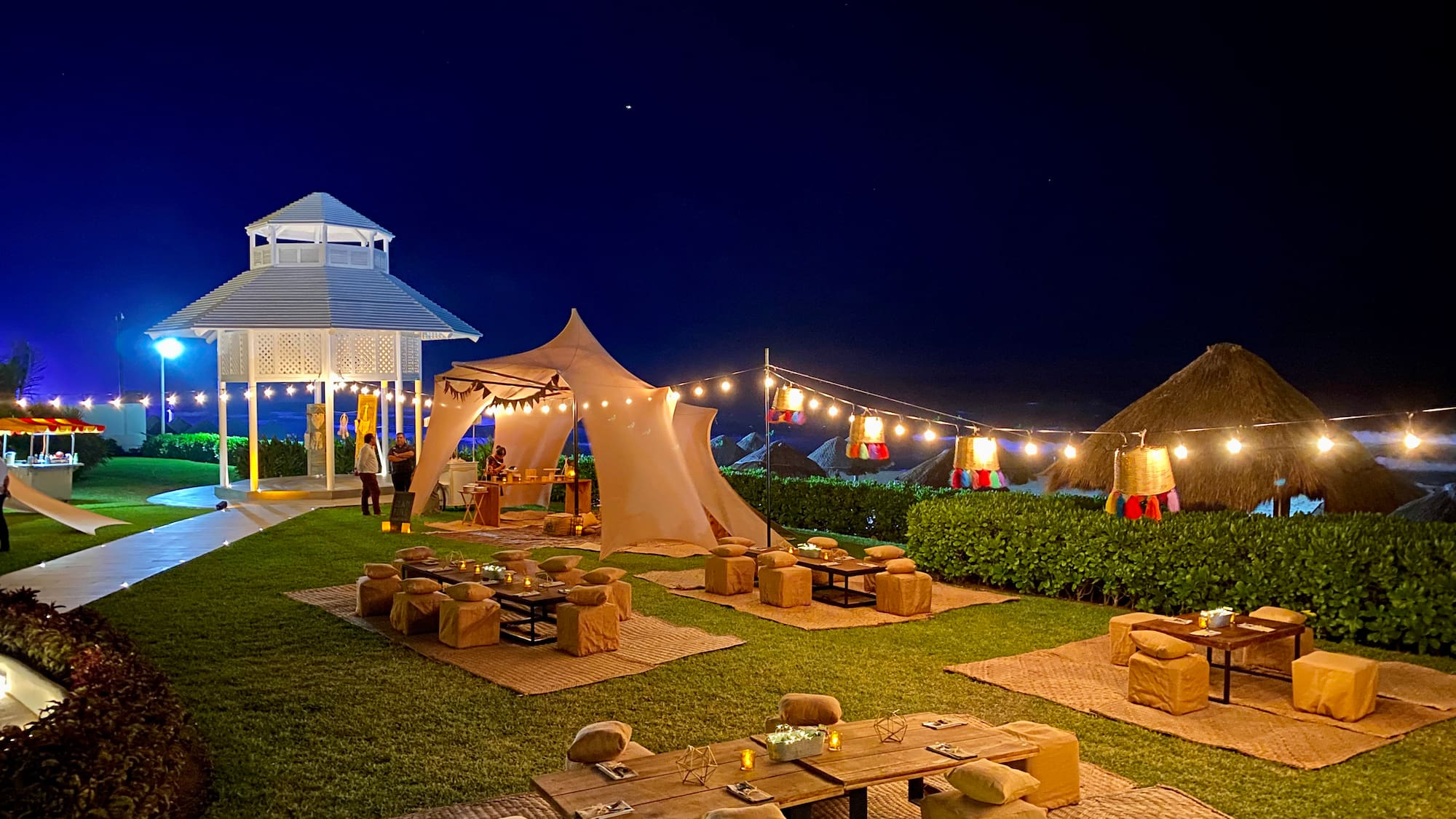 a group of tables and chairs in a yard with lights and a gazebo