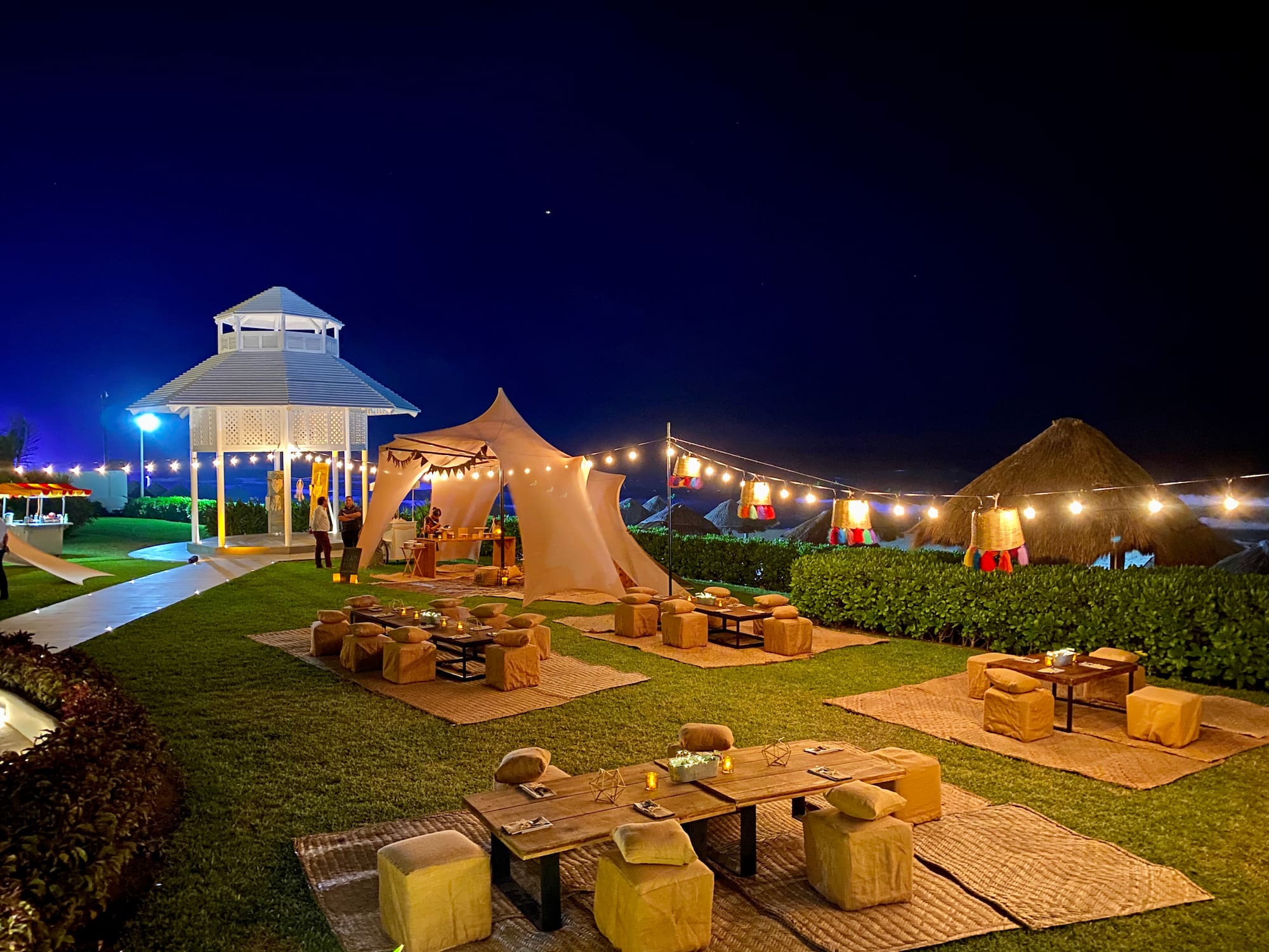 a group of tables and chairs in a yard with lights and a gazebo