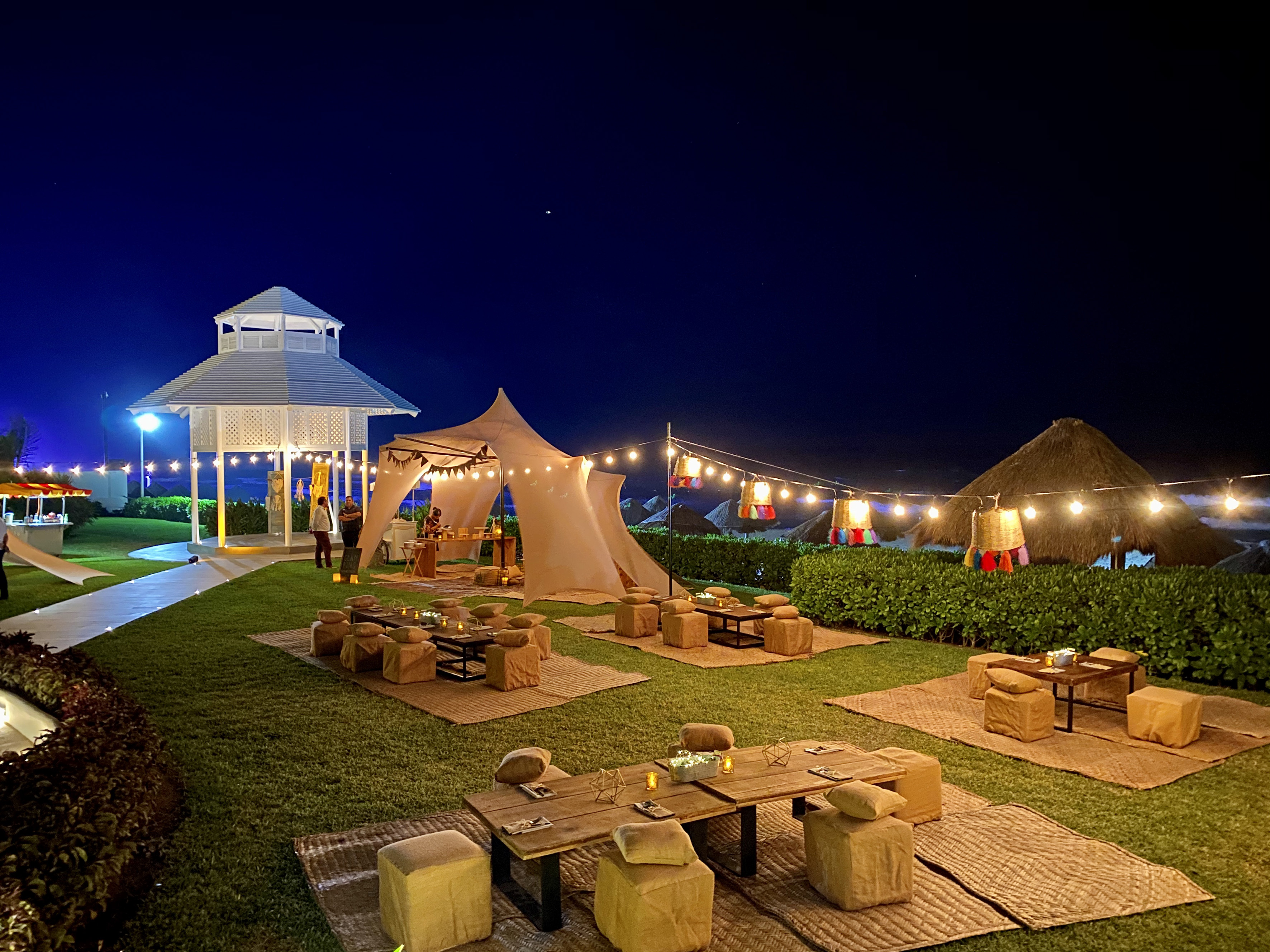 Nighttime outdoor lounge with string lights, white gazebo, and low seating.