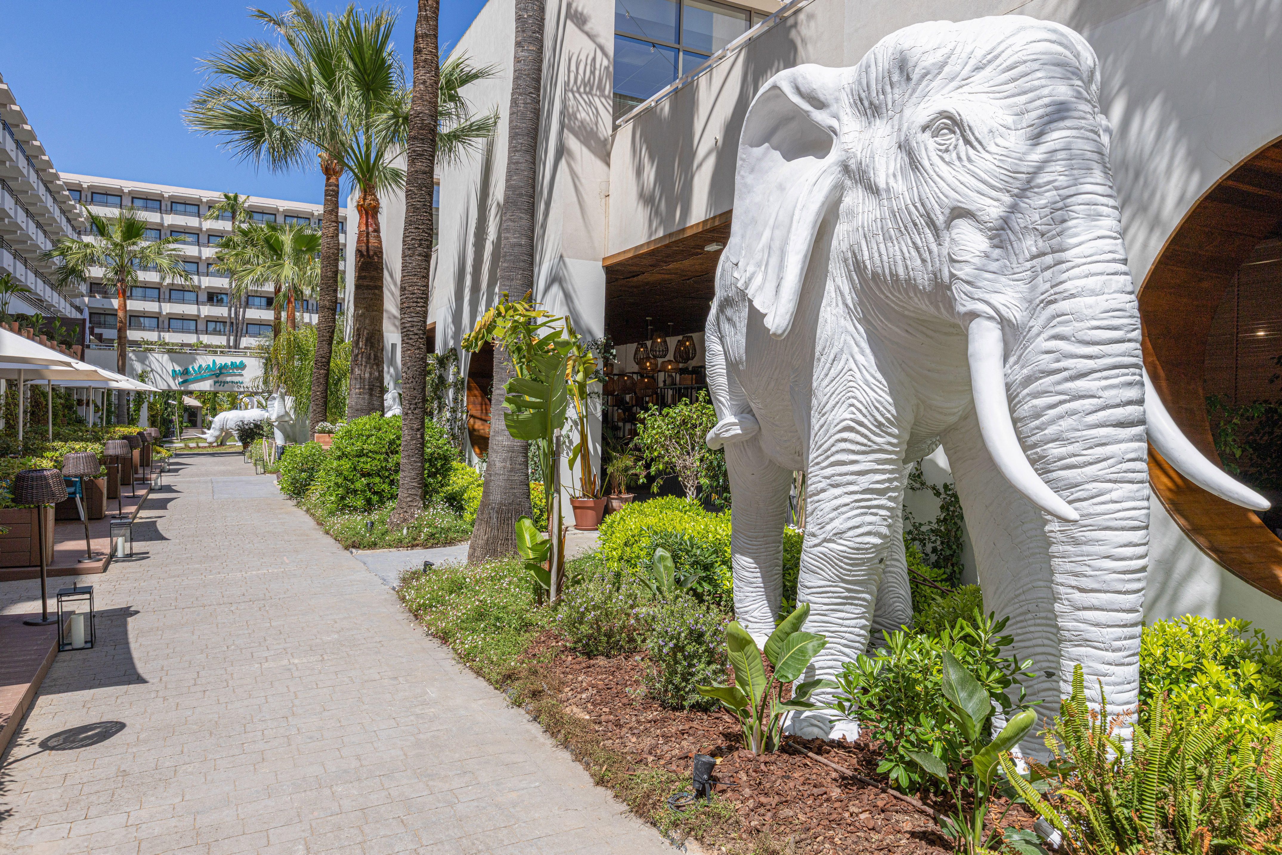 White elephant statue at a tropical resort entrance with palm trees and walkway.