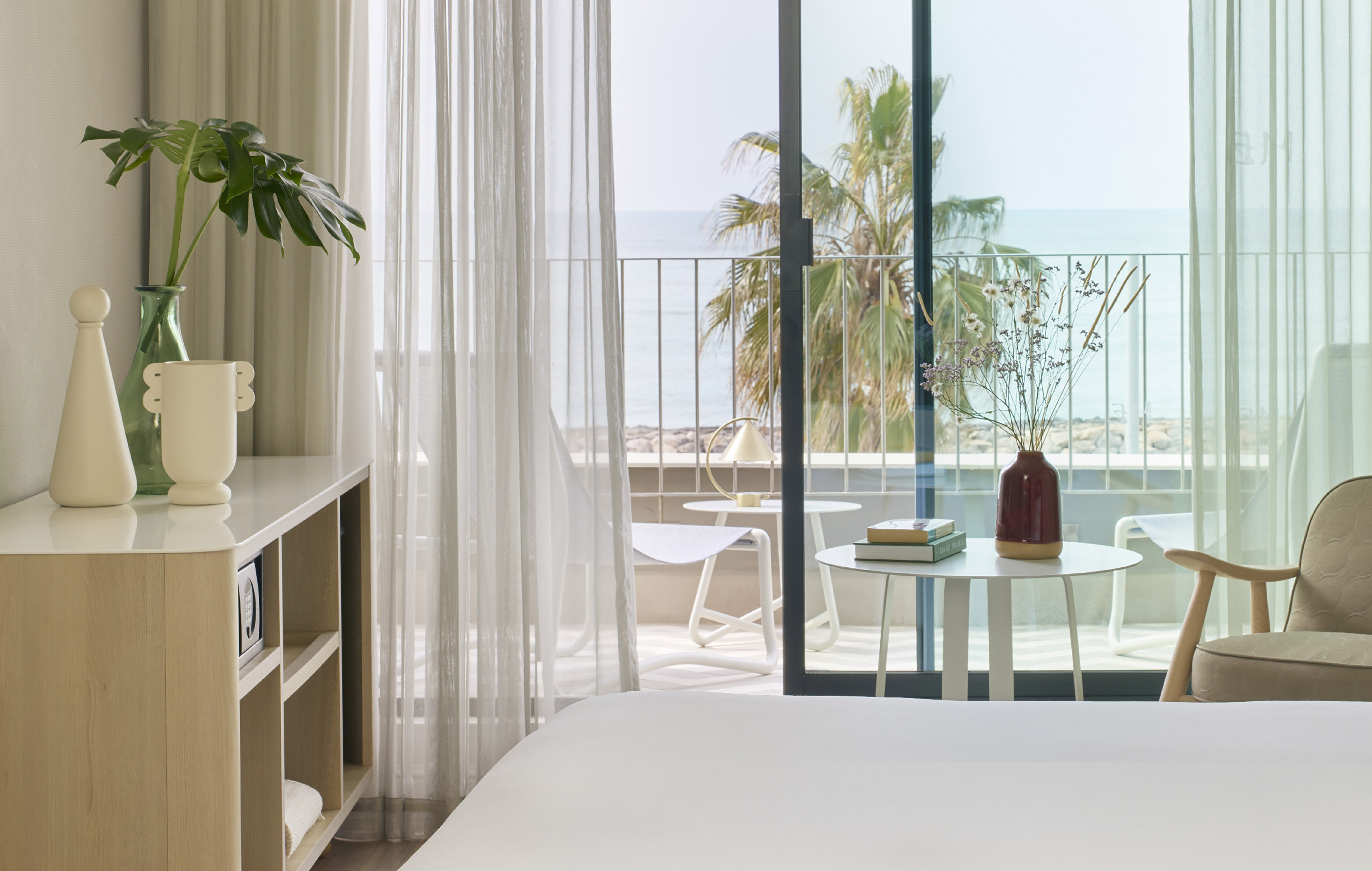 Modern hotel bedroom with ocean view balcony, palm trees, and elegant decor.