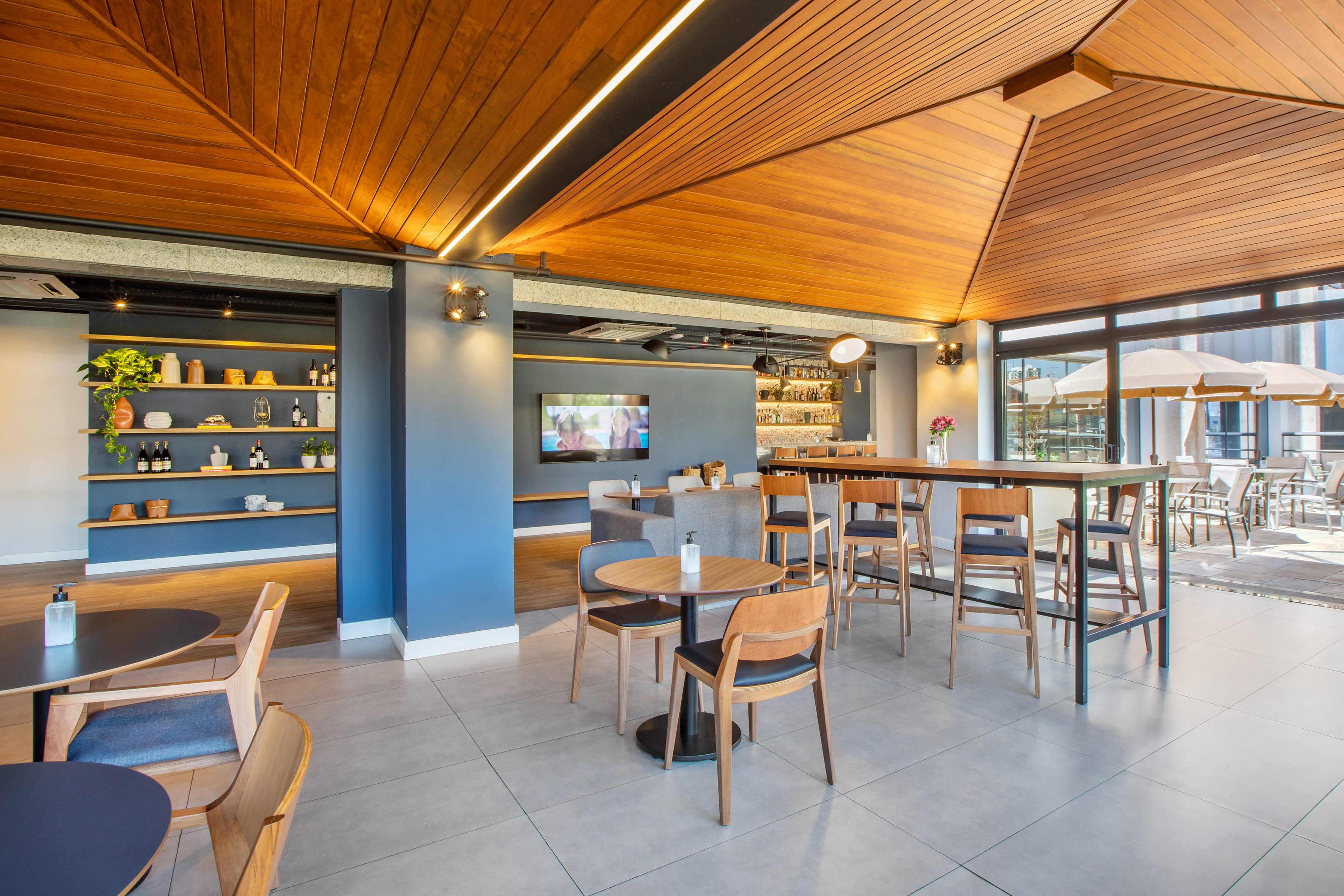 Modern restaurant bar interior with wooden ceiling, varied seating, and patio view.