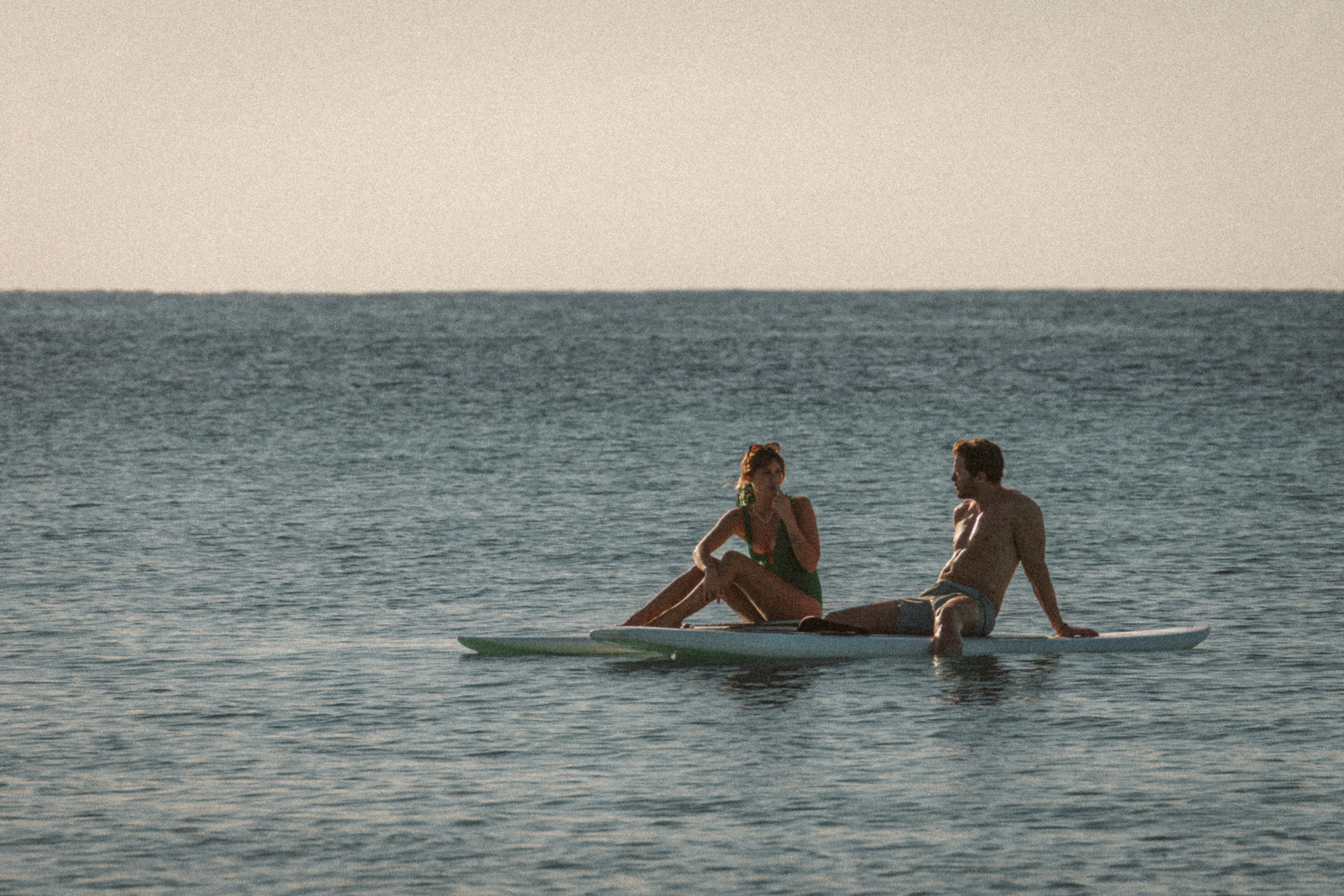 a man and woman sitting on surfboards in the water