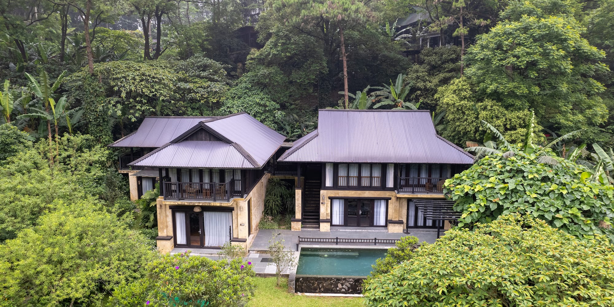 a two story house with a pool in the middle of trees