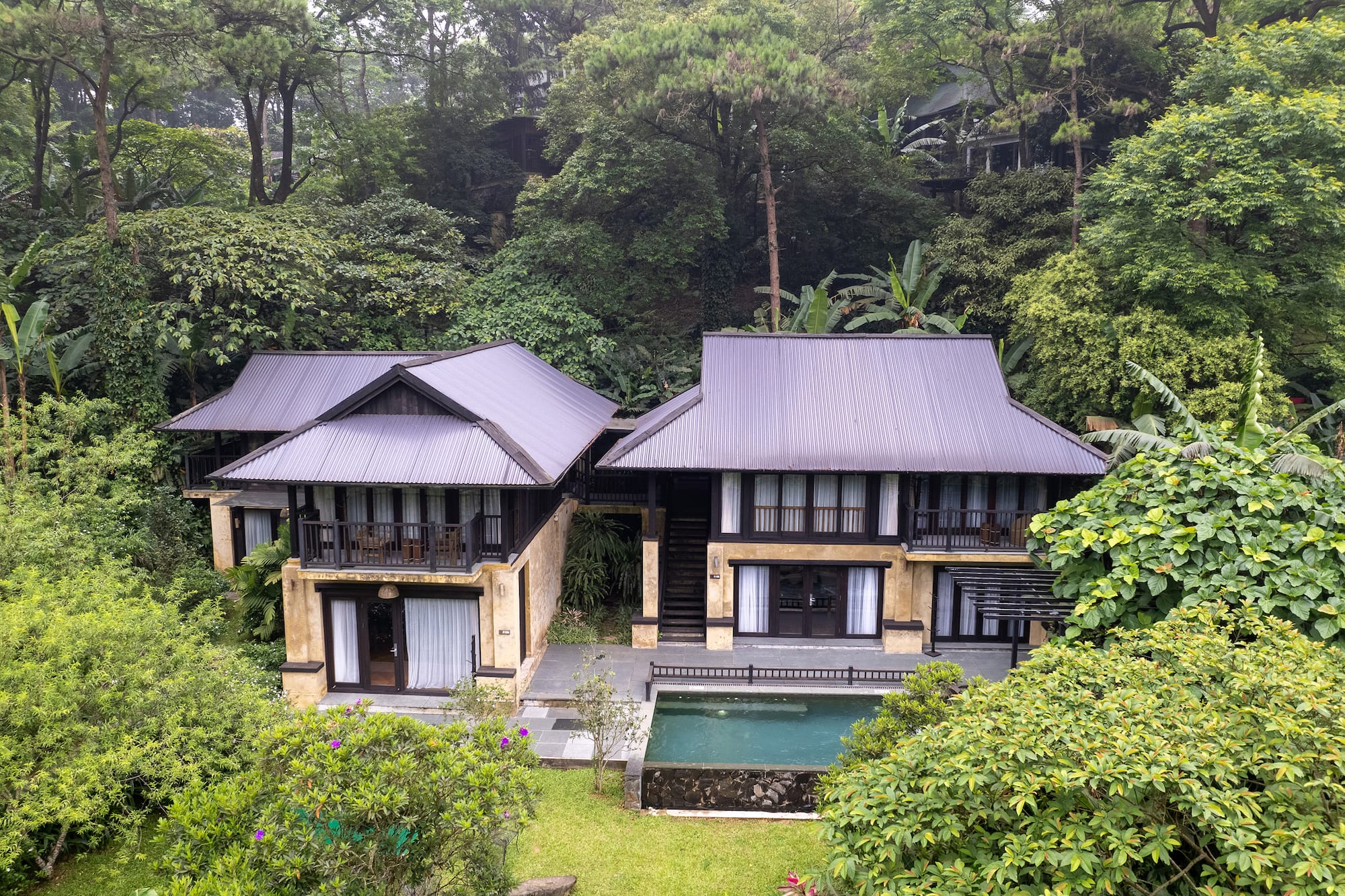 a two story house with a pool in the middle of trees