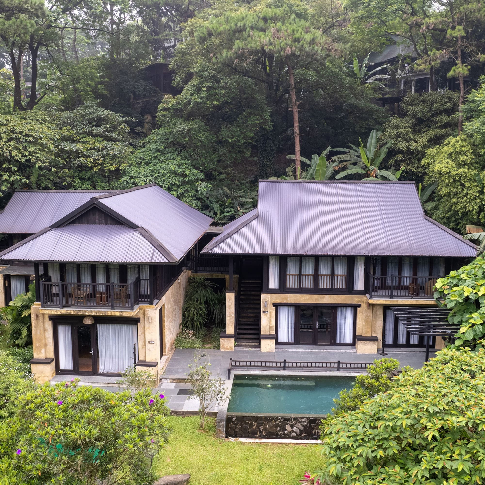a two story house with a pool in the middle of trees