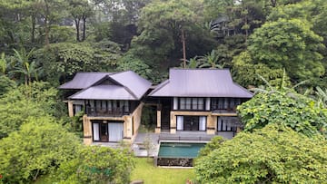 a two story house with a pool in the middle of trees