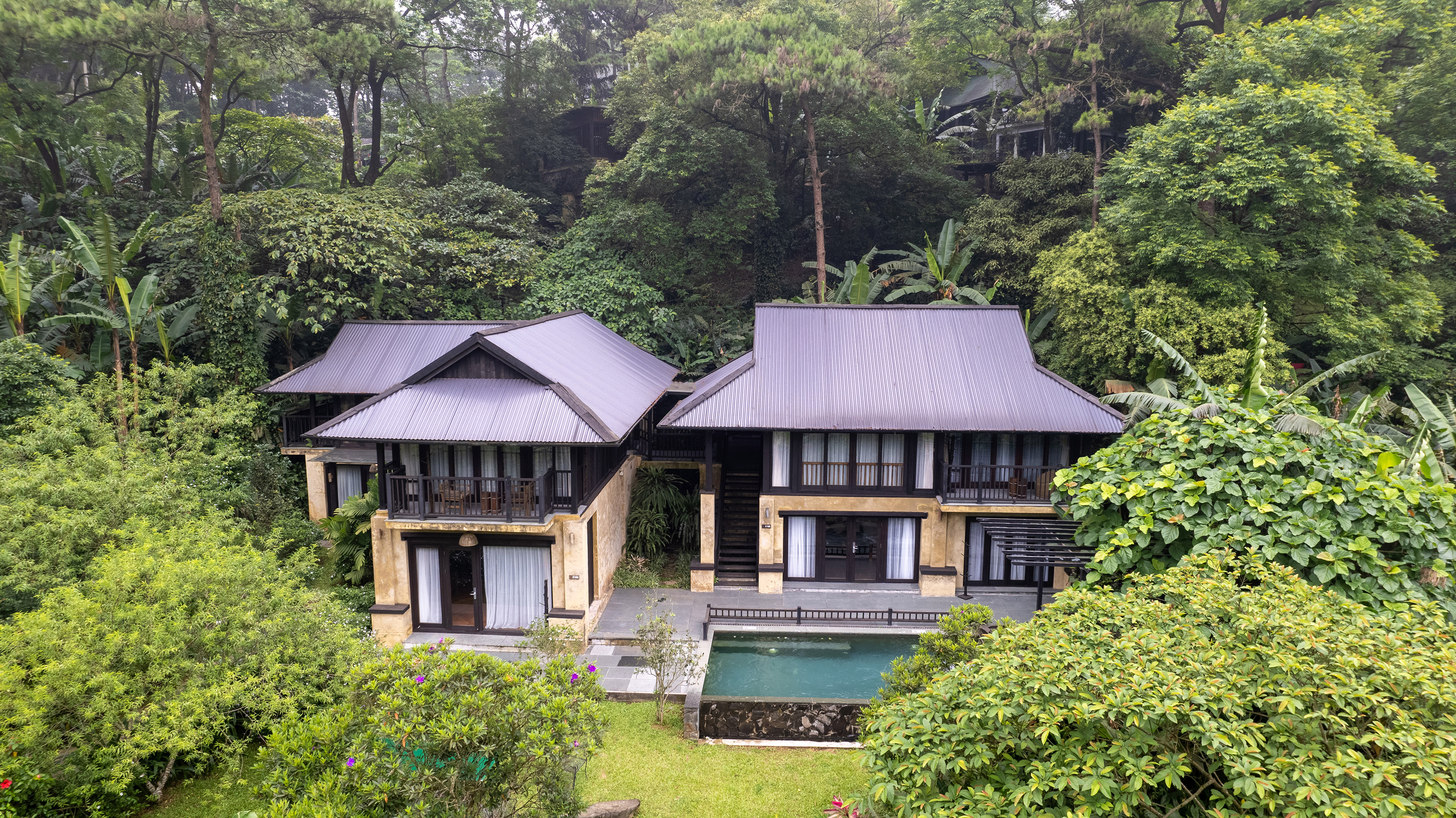 a two story house with a pool in the middle of trees