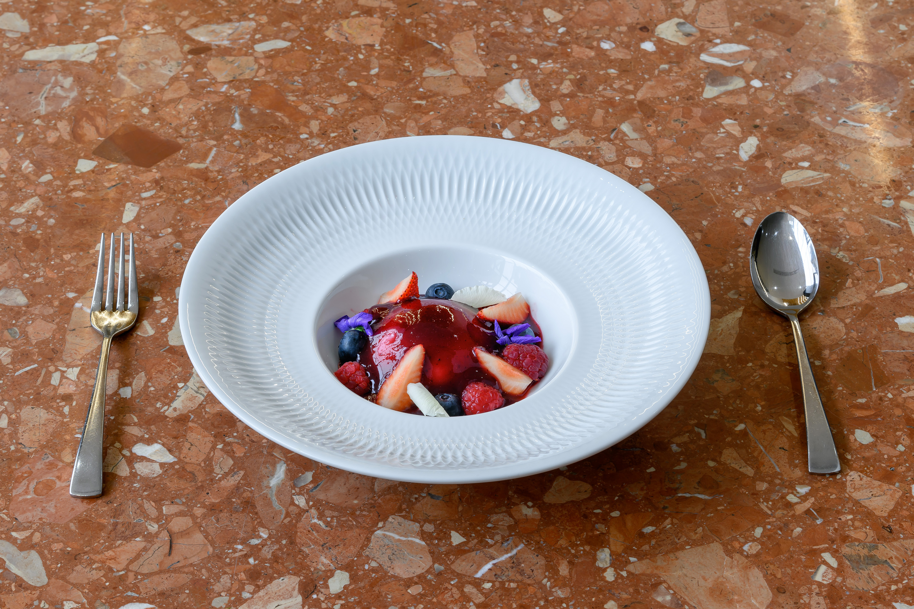 Berry dessert with red coulis, strawberries, blueberries, raspberries, and edible flowers.