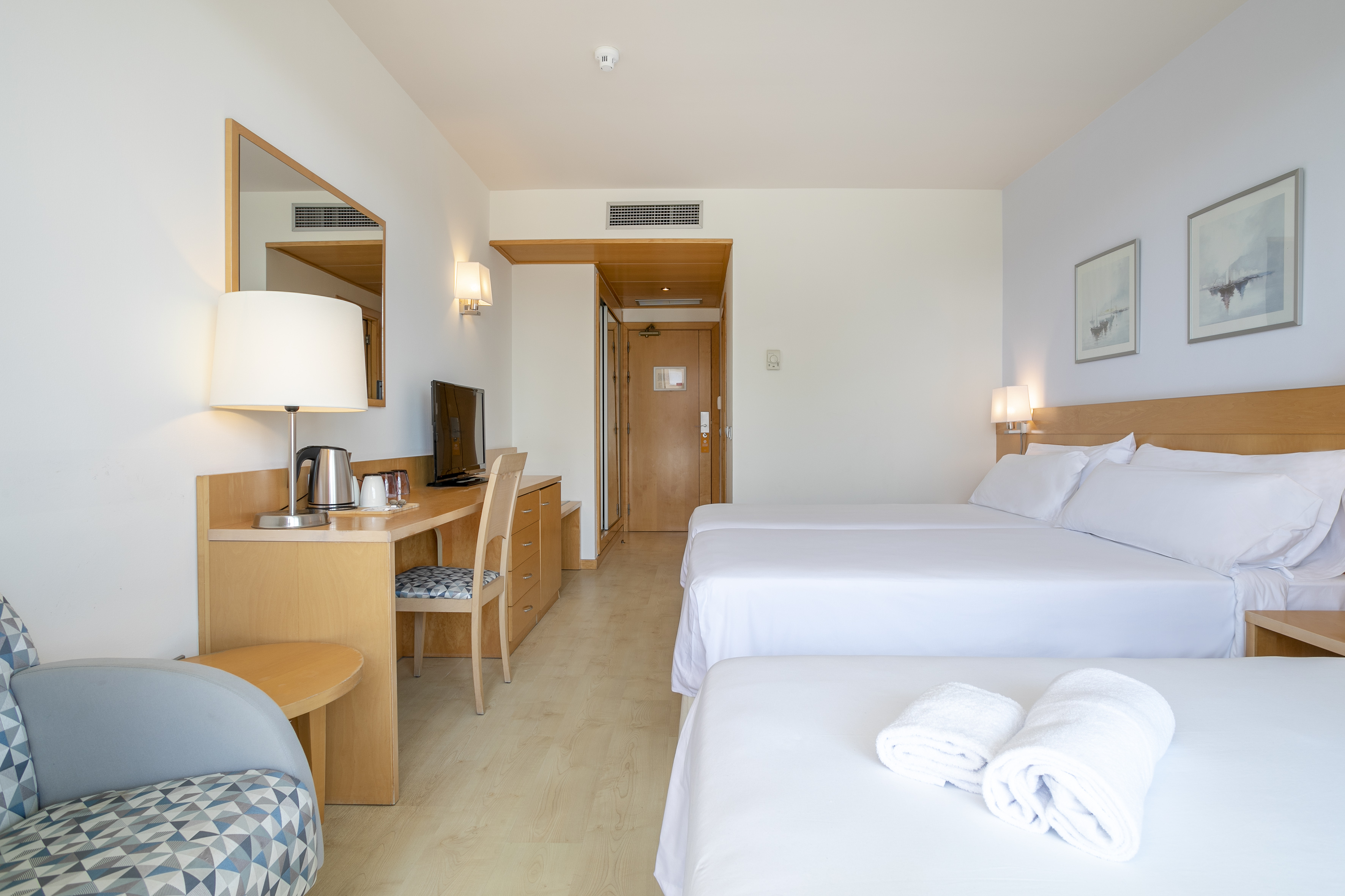 Hotel room with two single beds, white linens, wooden desk, and TV.