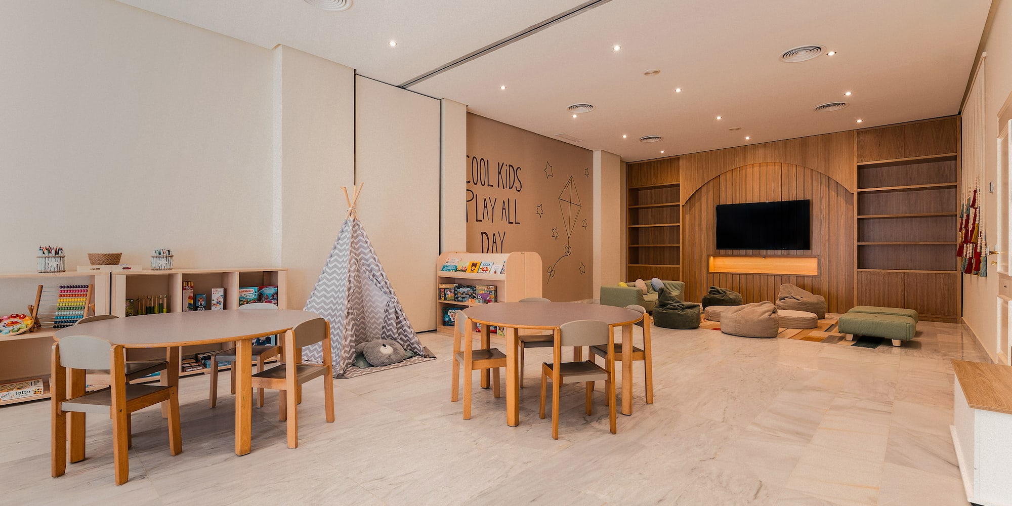 Kids' room with tables, teepee, beanbags, books, and playful wall decor.