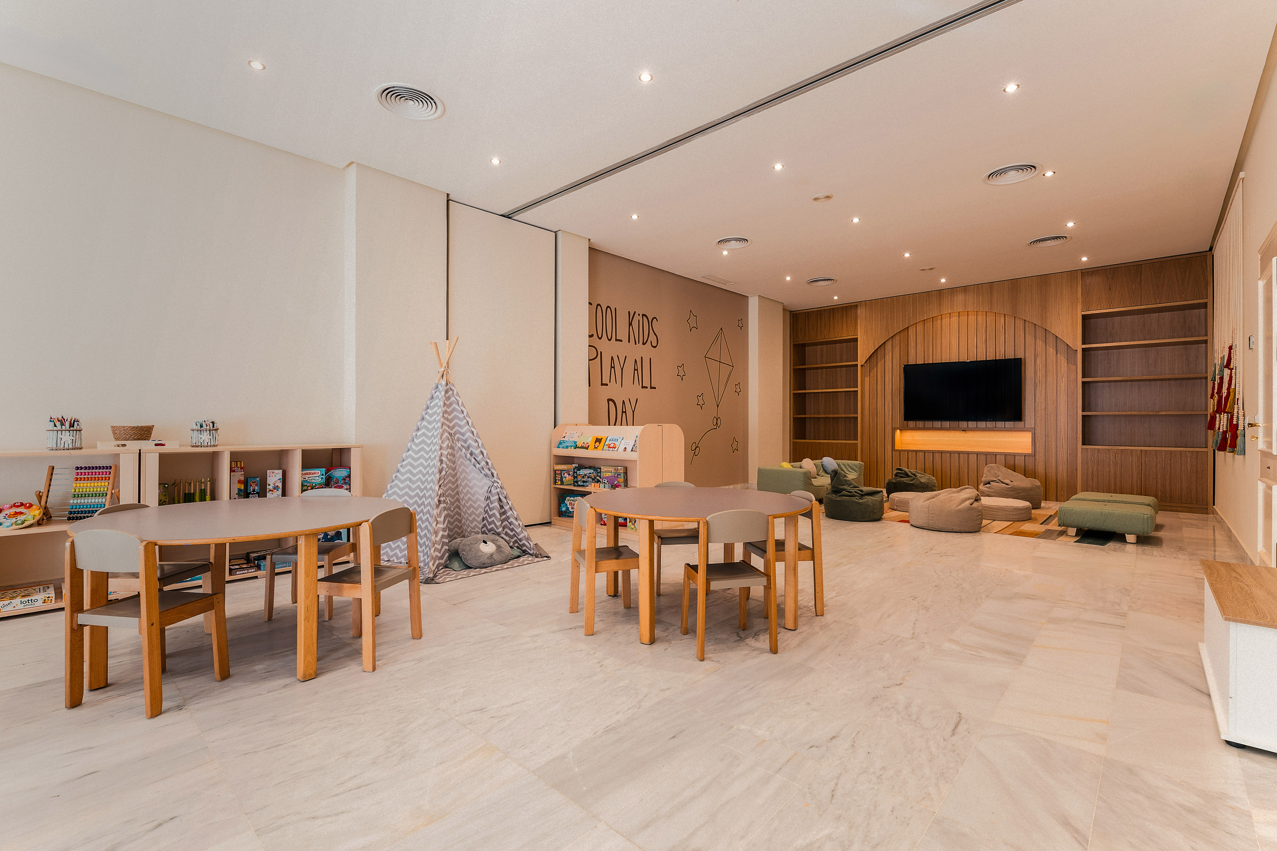 Kids' room with tables, teepee, beanbags, books, and playful wall decor.