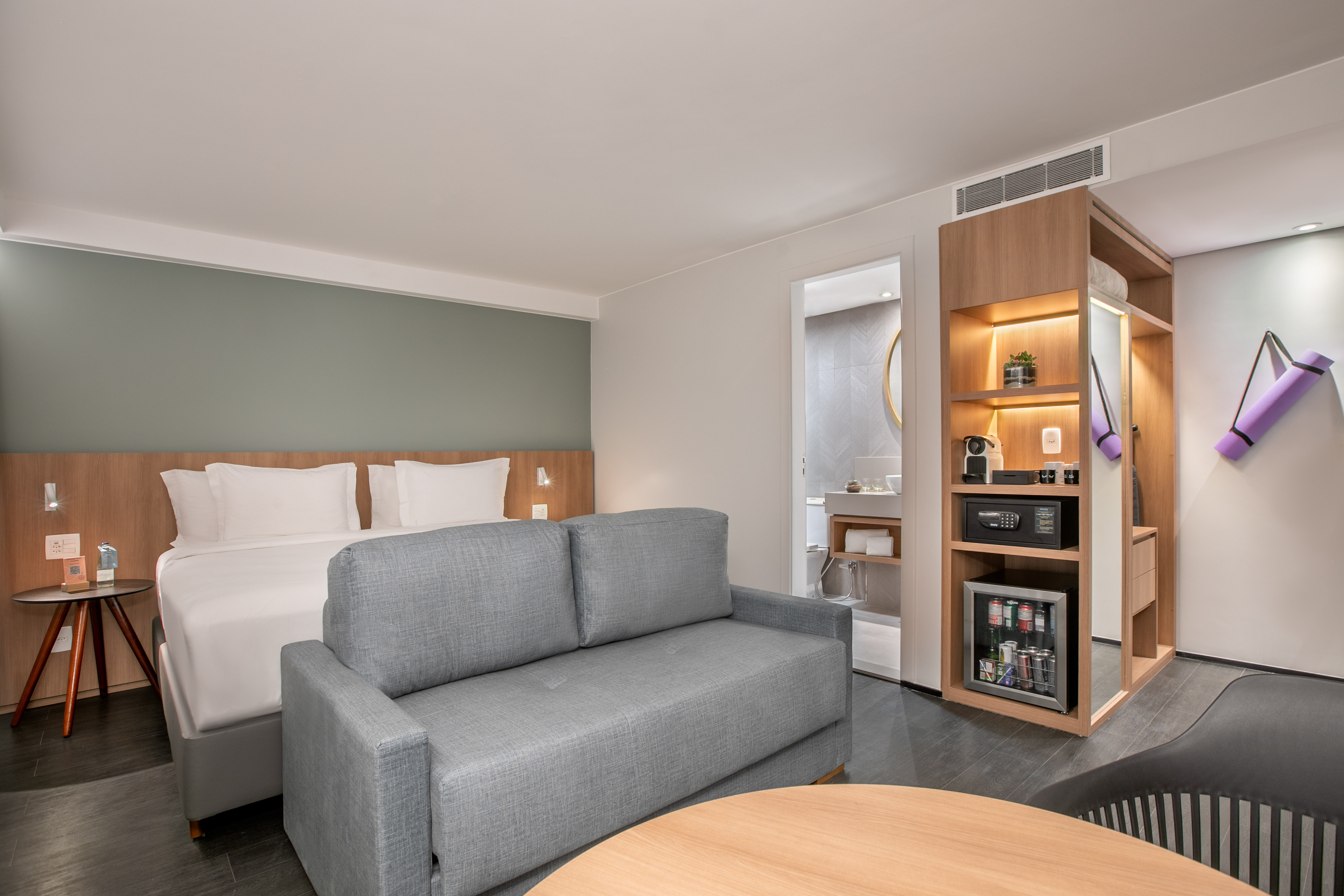 Bright hotel suite with bed, sofa bed, mini-fridge, coffee maker, and yoga mat.