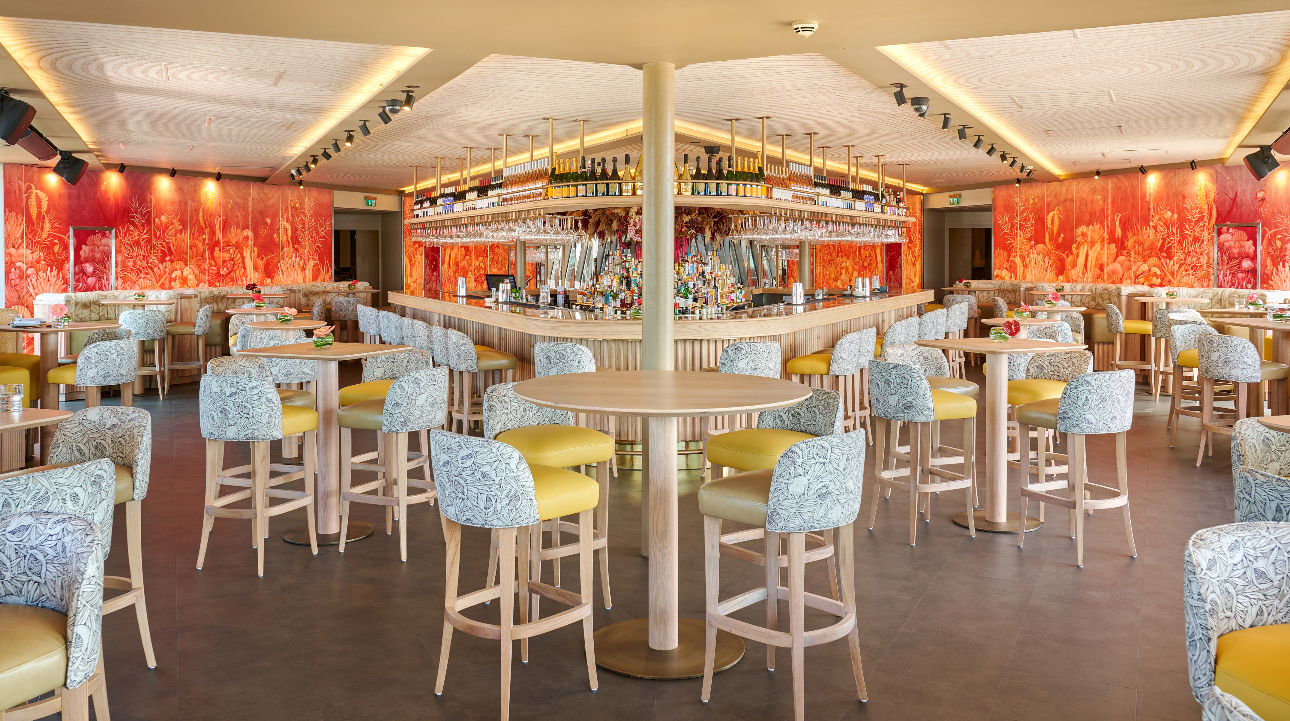 Vibrant tropical bar with orange botanical walls and patterned high-top seating.