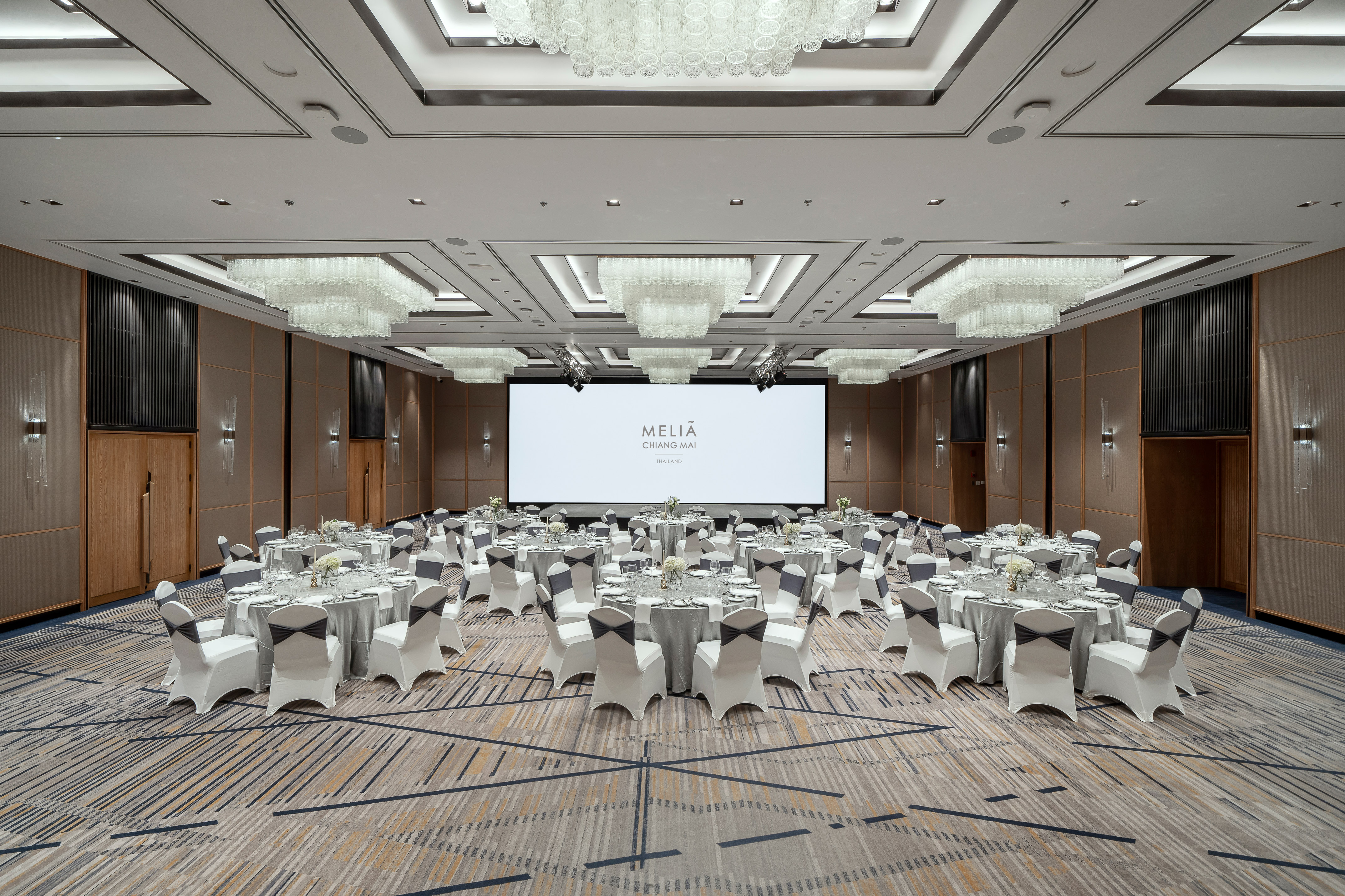 Meliá Chiang Mai hotel ballroom with round tables, white chairs, and large screen.
