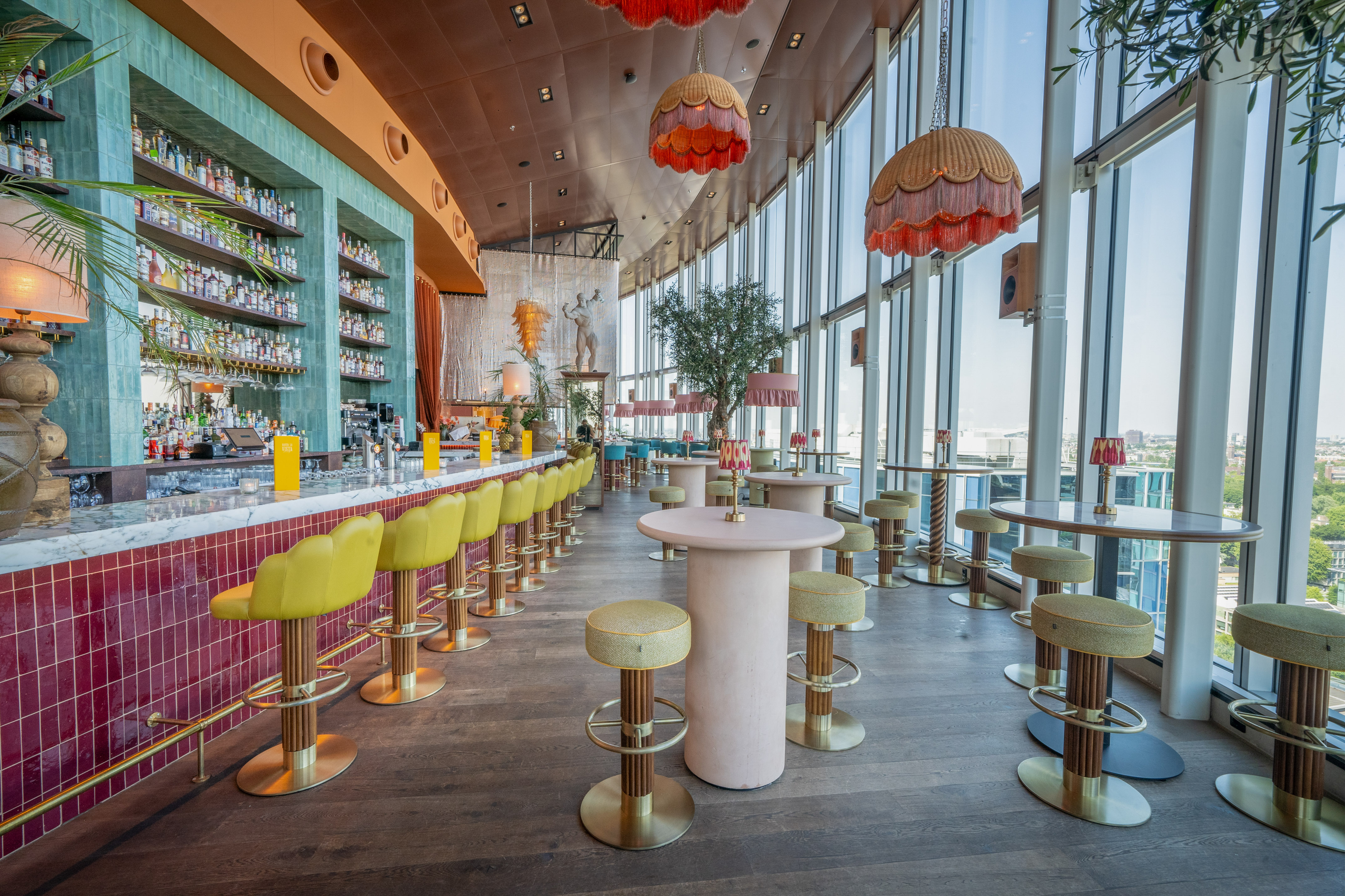 Stylish rooftop bar with city views, vibrant decor, and long bar area.
