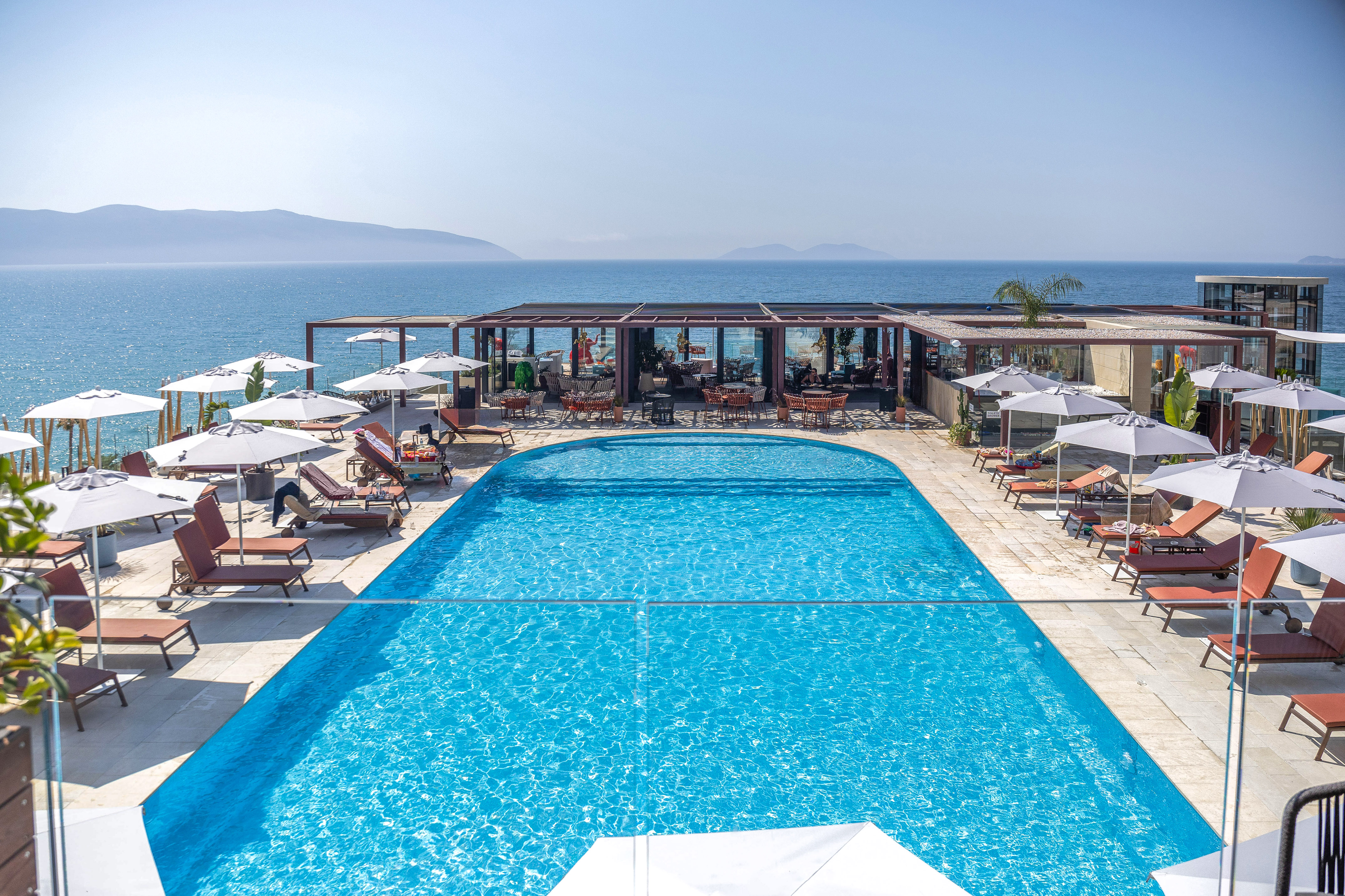 Resort swimming pool with sea view, sun loungers & outdoor dining.