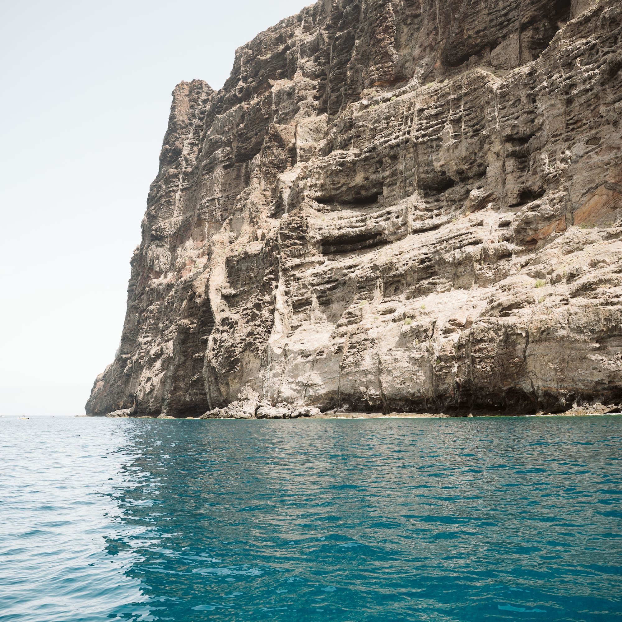 Massive textured rock cliff rising from clear blue ocean water.