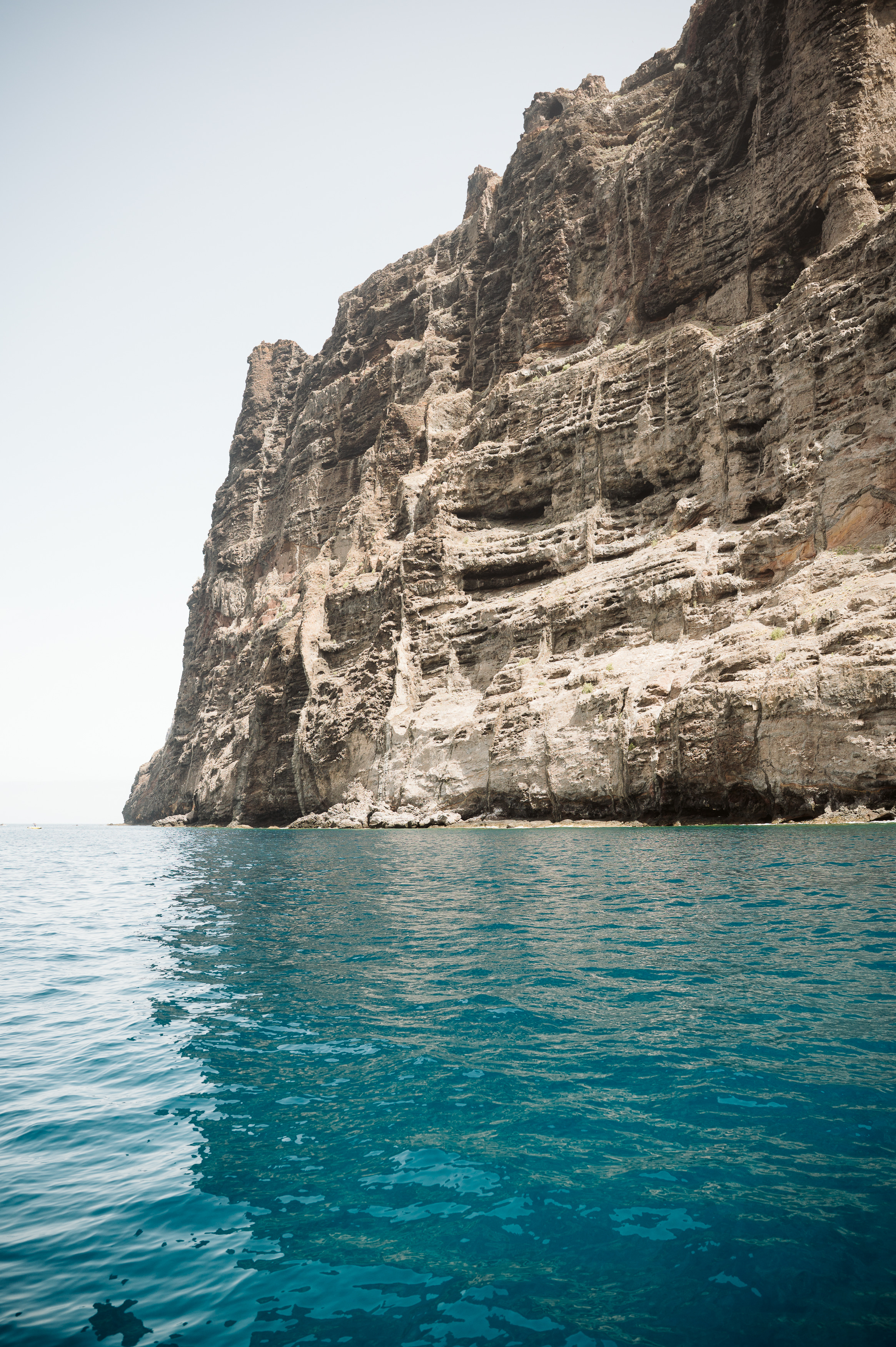 Massive textured rock cliff rising from clear blue ocean water.