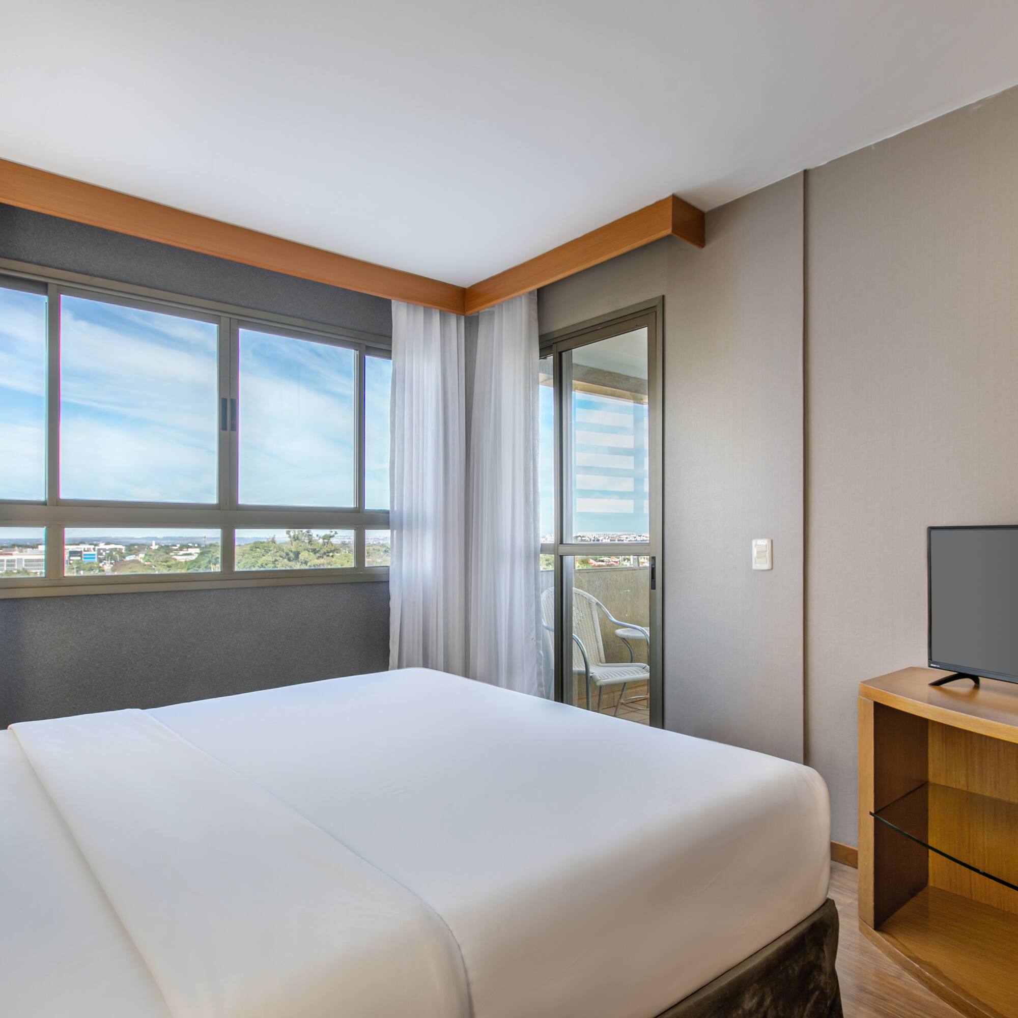 Modern hotel bedroom with king bed, balcony, city view, and TV.