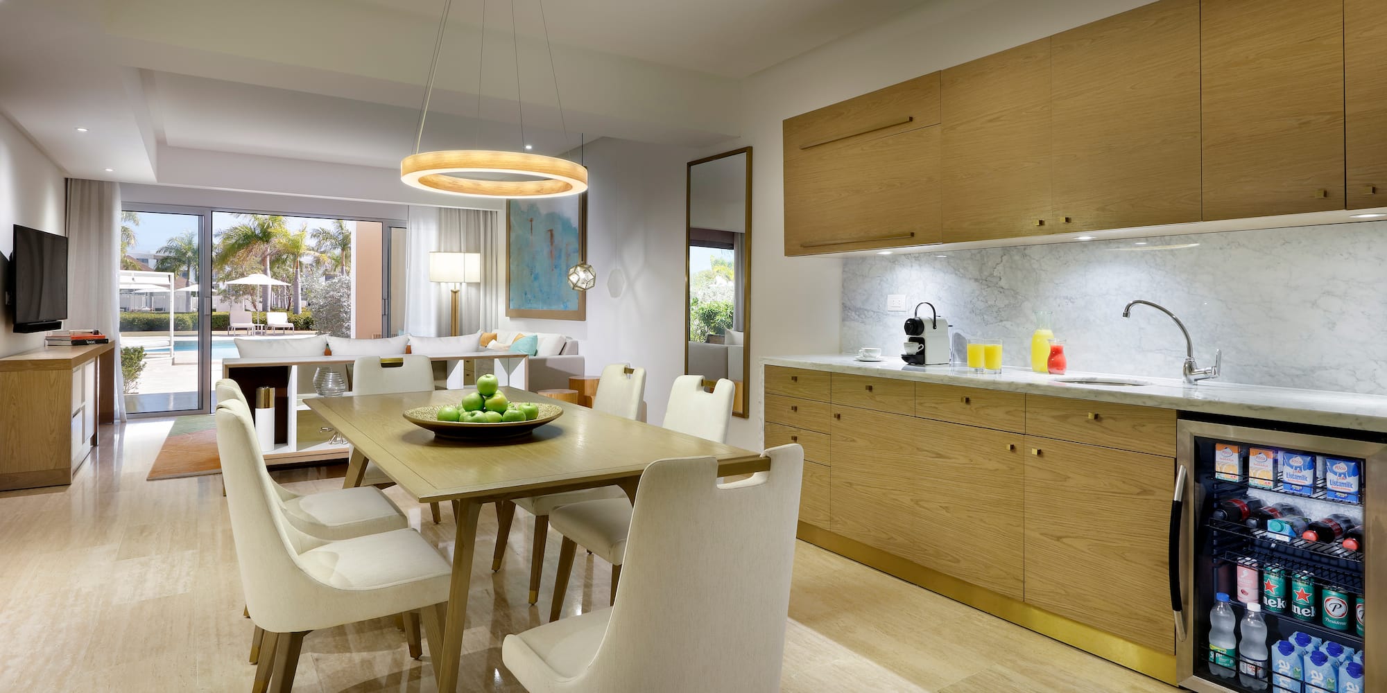 Modern resort suite: dining, kitchenette, living area, and pool view.