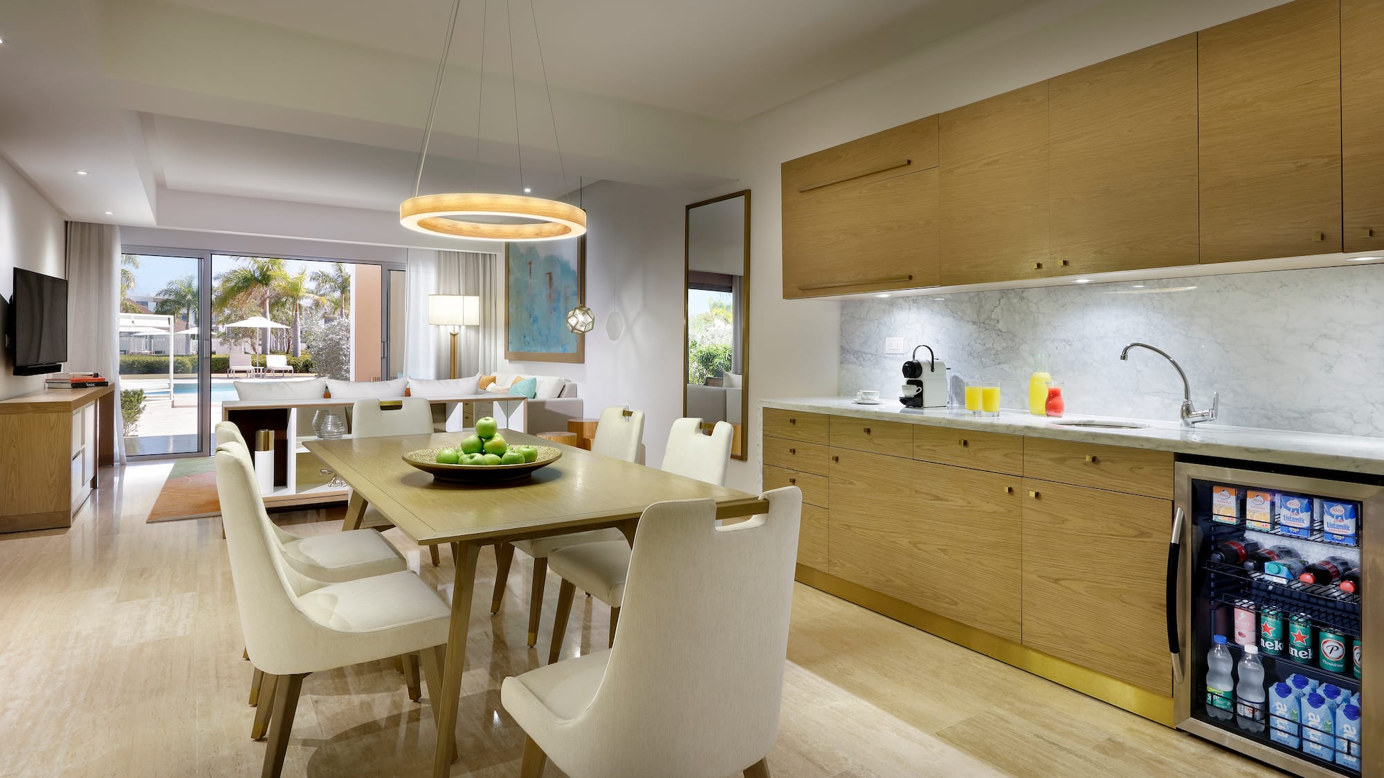 Modern resort suite: dining, kitchenette, living area, and pool view.